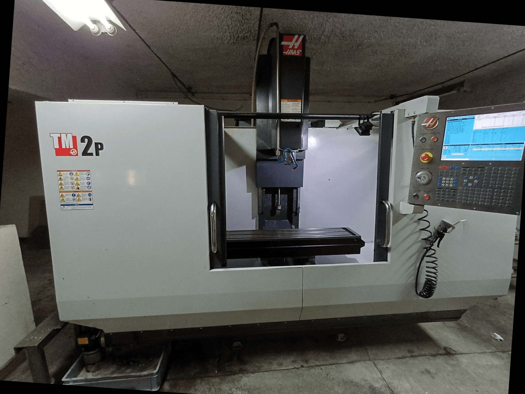 HAAS TM-2P függőleges megmunkálóközpont, előlnézet, a vezérlőpanel, az orsófej és a gépágy látható.
