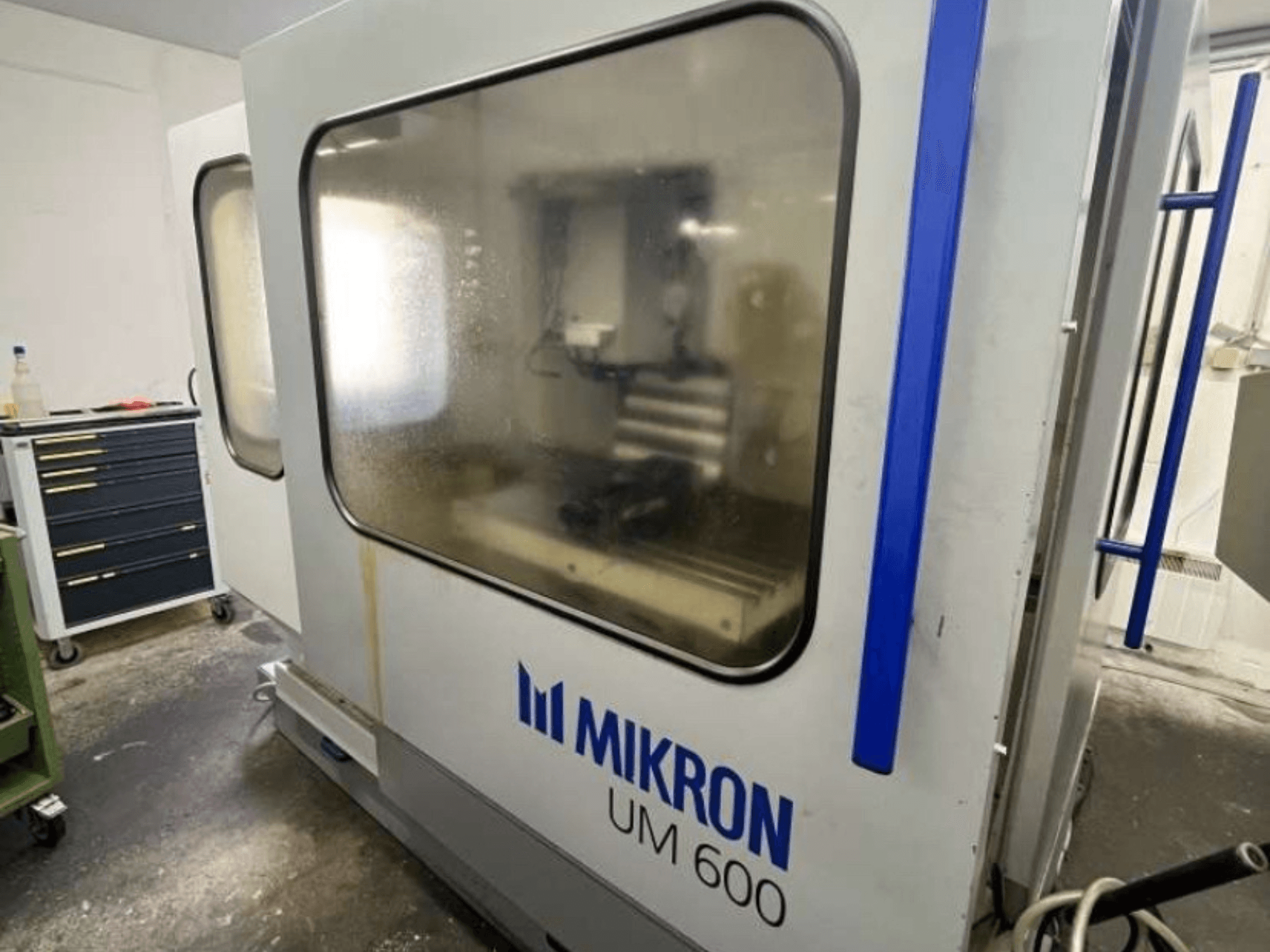 MIKRON UM 600 TNC 410/426 univerzális megmunkálóközpont, oldalnézet, ködös üveggel és látható szerszámtárolóval a közelben.