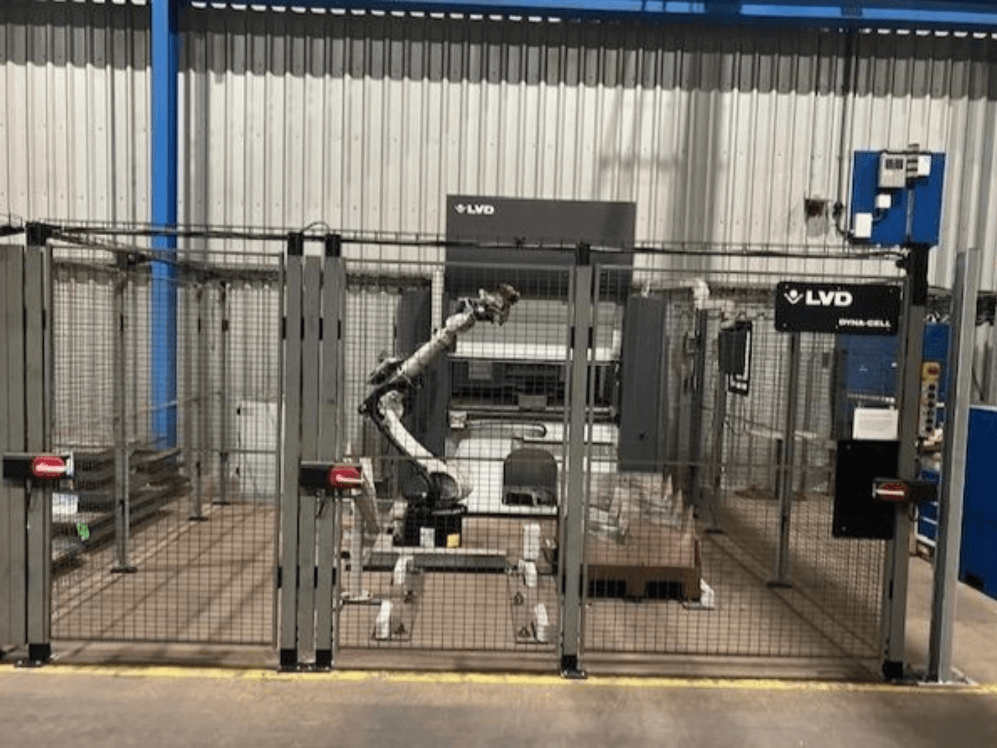 LVD Dyna-Cell robotikus munkaállomás egy elkerített burkolatban, elölnézetben, a robotkarral és a vezérlőpanellel.