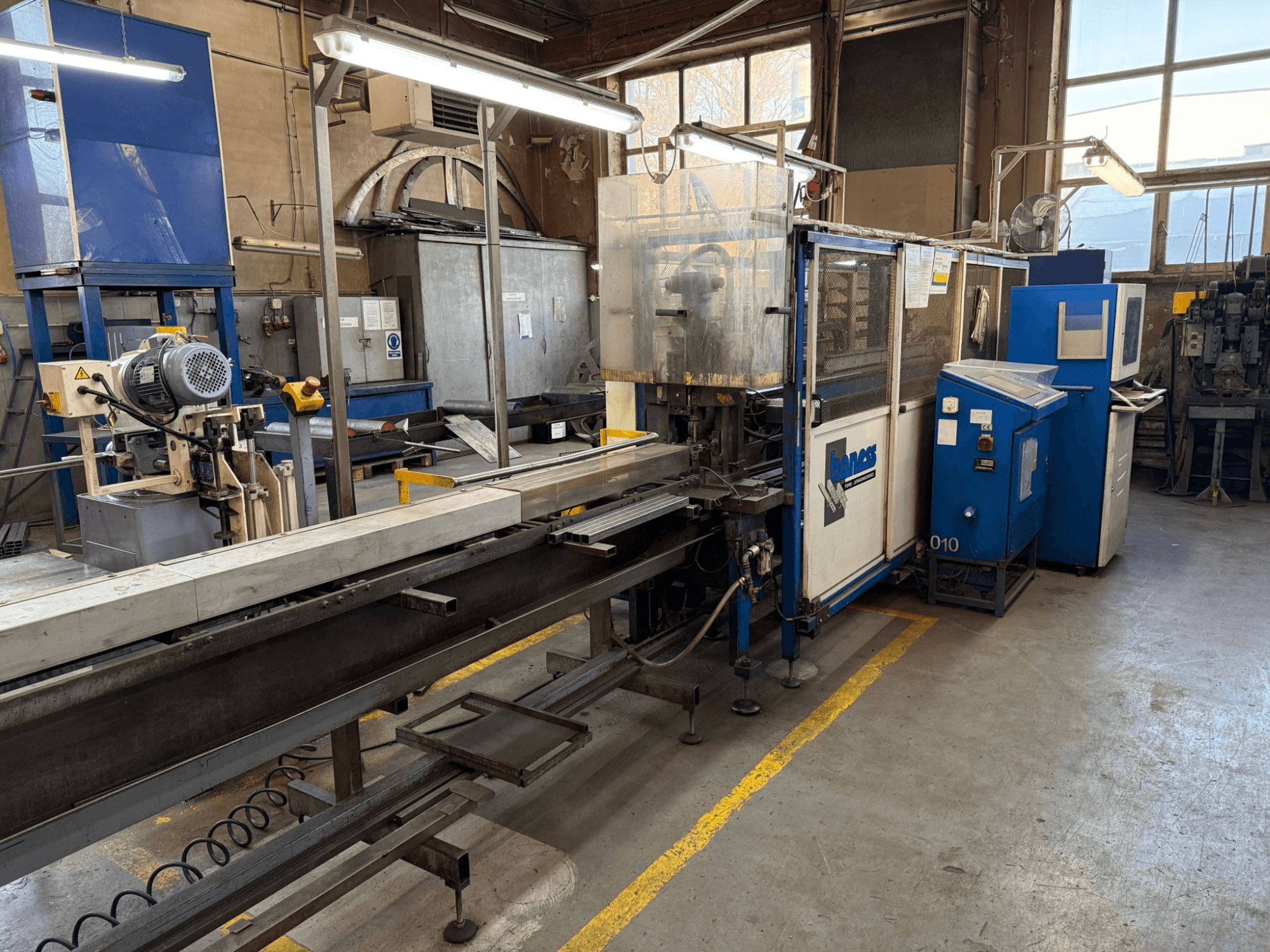 Ipari műhely egy kék Haweas géppel, oldalnézetben a szállítószalag és a berendezés egy nagy, jól megvilágított térben.