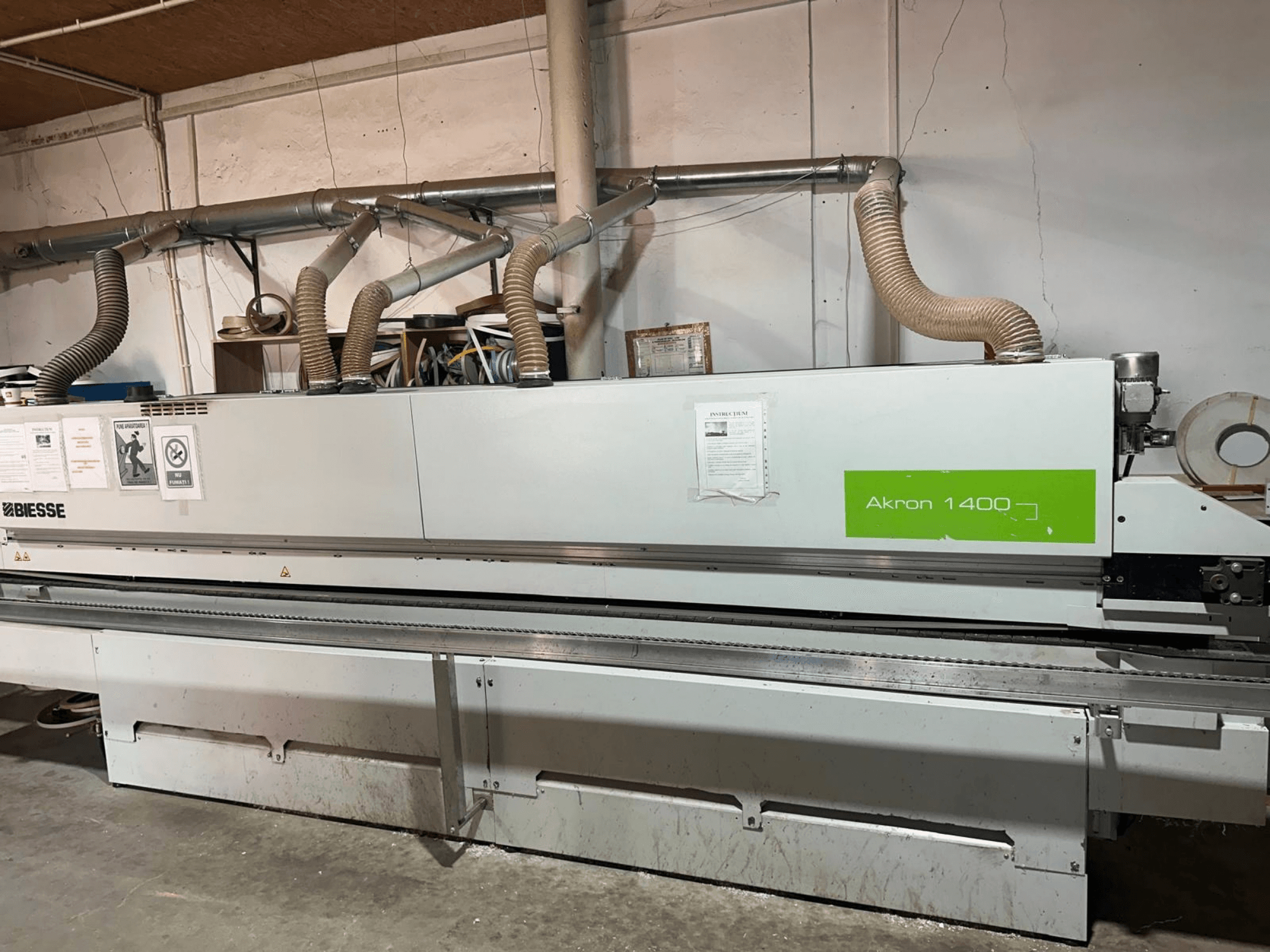 A BIESSE Akron 1440 A élragasztó gép oldalnézetben, a légcsatornákkal, a kezelőpanellel és a működési matricákkal együtt.