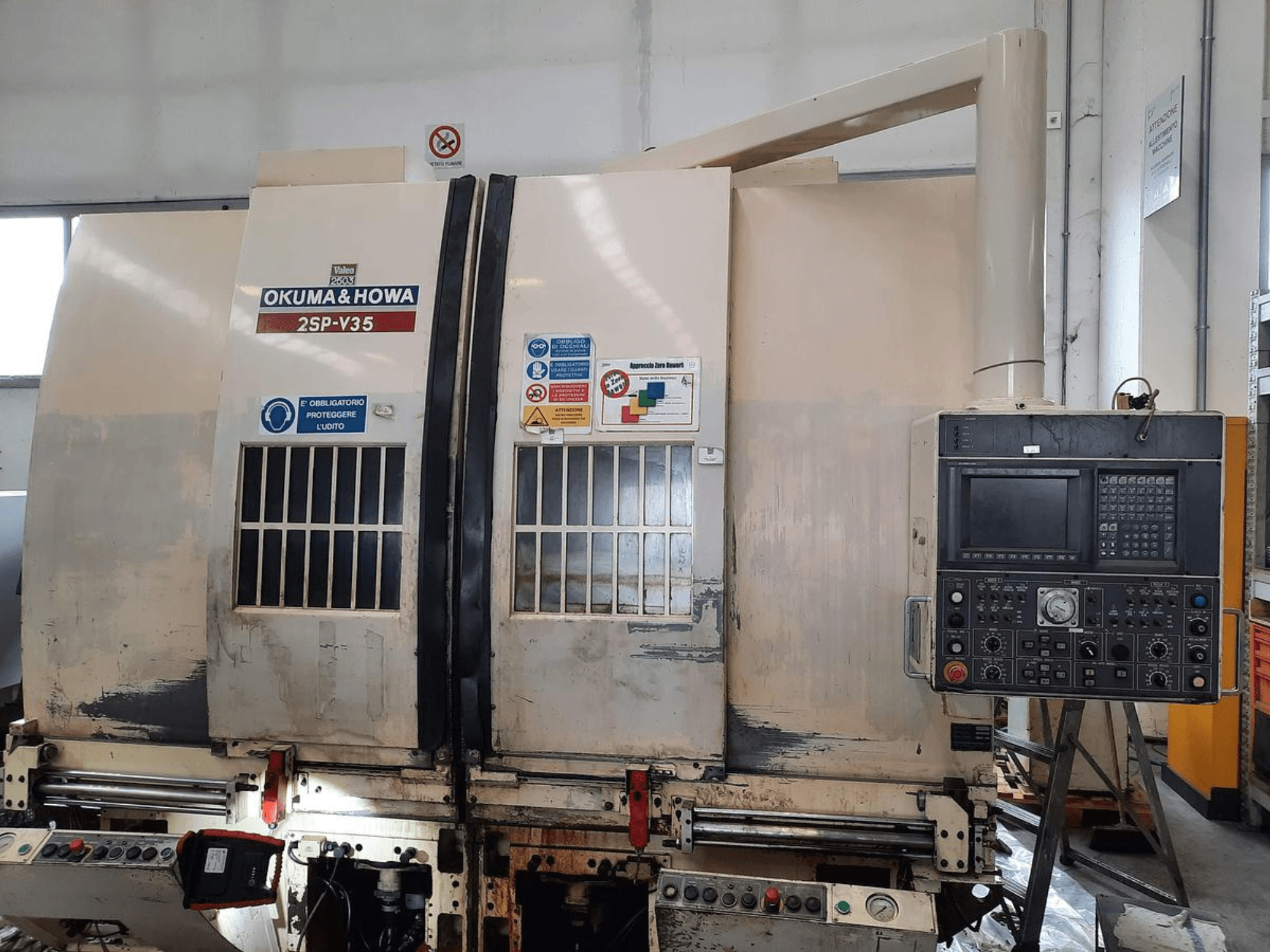 OKUMA & HOWA 2SP-V35 CNC-gép elölről nézve, a különböző gombokkal és biztonsági címkékkel ellátott vezérlőpanellel.