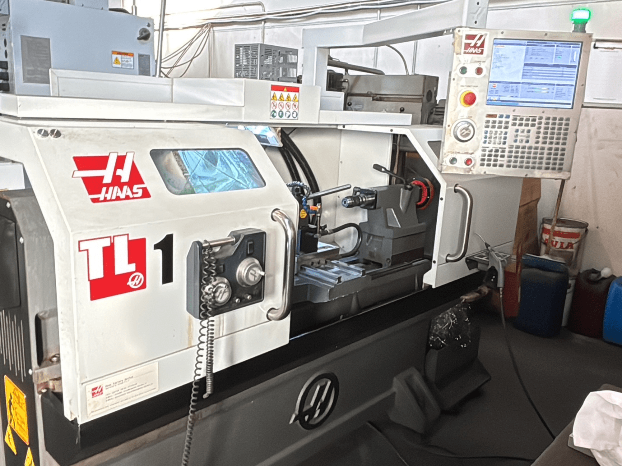Haas TL-1 CNC esztergagép, előlnézet, kijelzővel ellátott vezérlőpanel, szerszámtartó és biztonsági címkék.