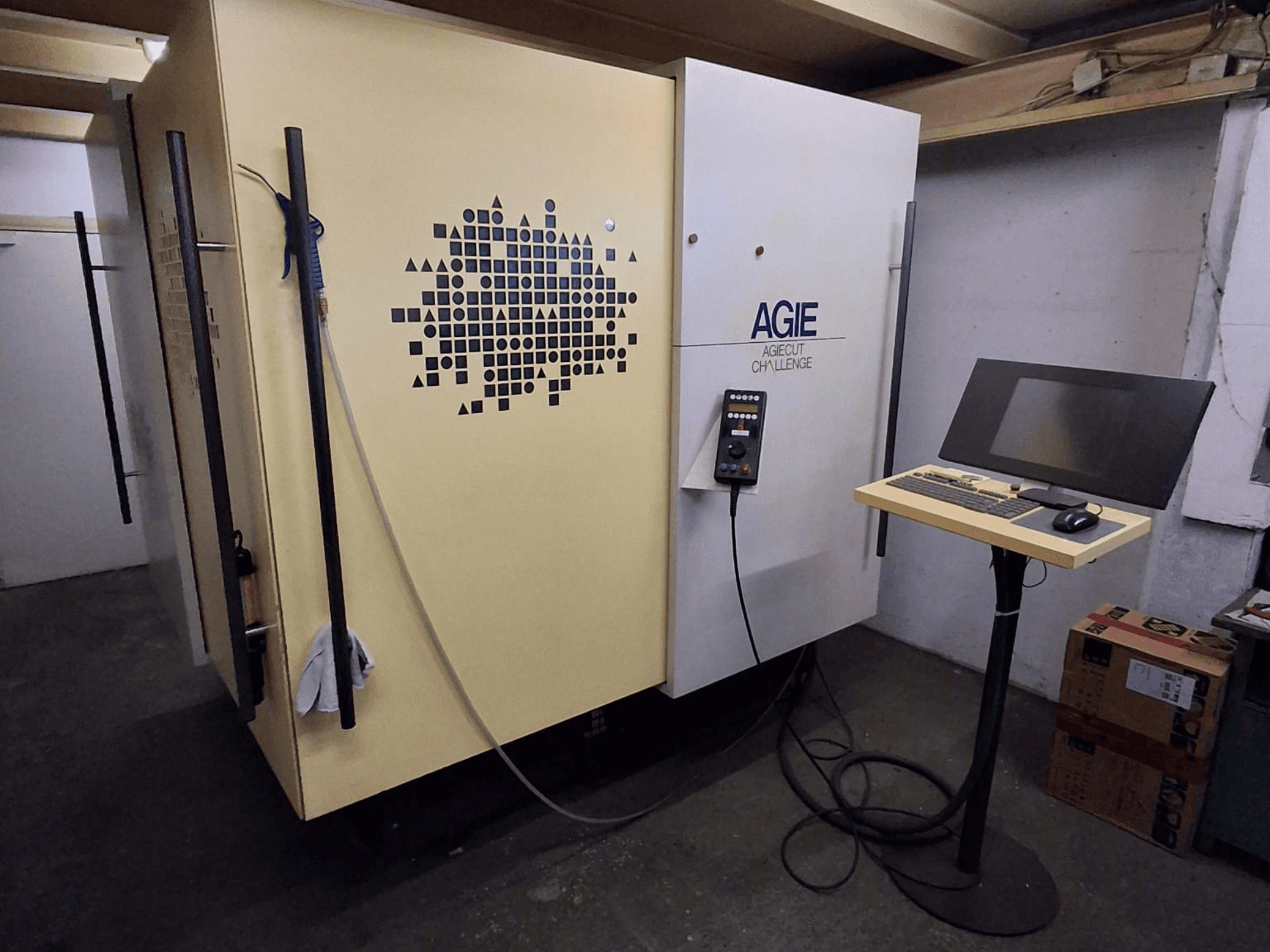 AGIE Agiecut Challenge kétvezetékes szikraforgácsoló gép egy műhelyben, állványon elhelyezett vezérlőpanellel és monitorral, elölnézetből.