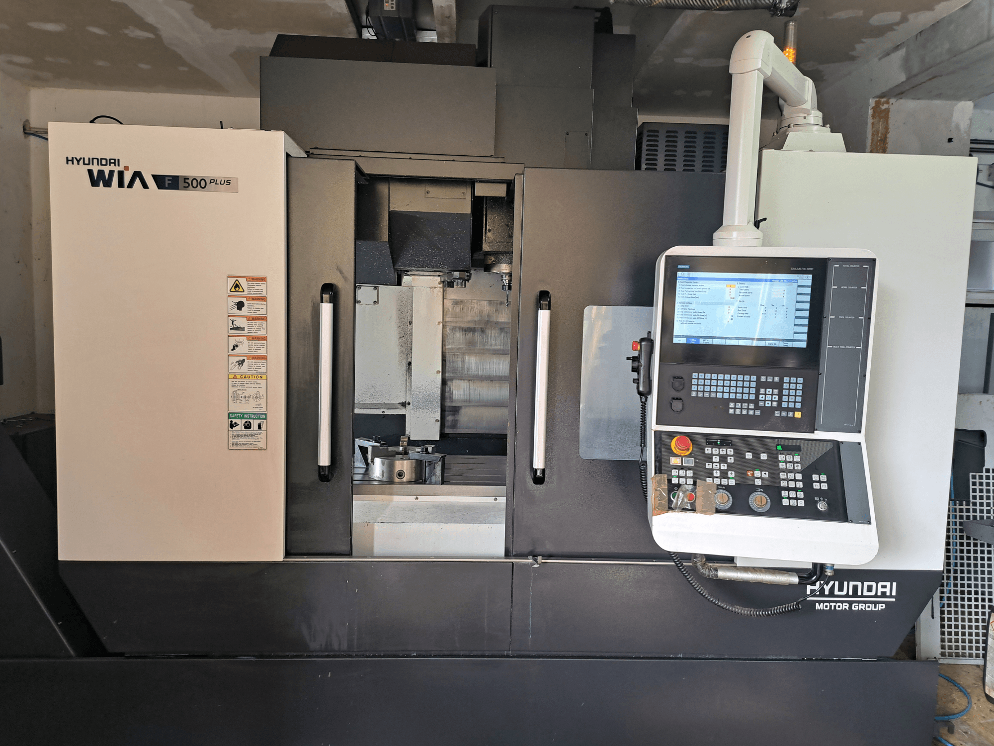 Hyundai WIA F500 Plus CNC-gép elölnézetben, digitális vezérlőpanellel és biztonsági címkékkel.
