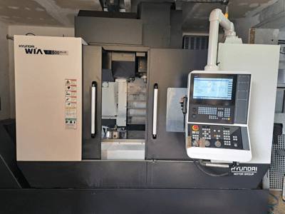 Hyundai WIA F500 Plus CNC-gép elölnézetben, digitális vezérlőpanellel és biztonsági címkékkel.