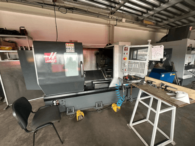Haas CNC eszterga (ST-10 modell) egy műhelyben, oldalnézetben a kezelőszervek, a szerszámok a munkapadon és egy szék a közelben.