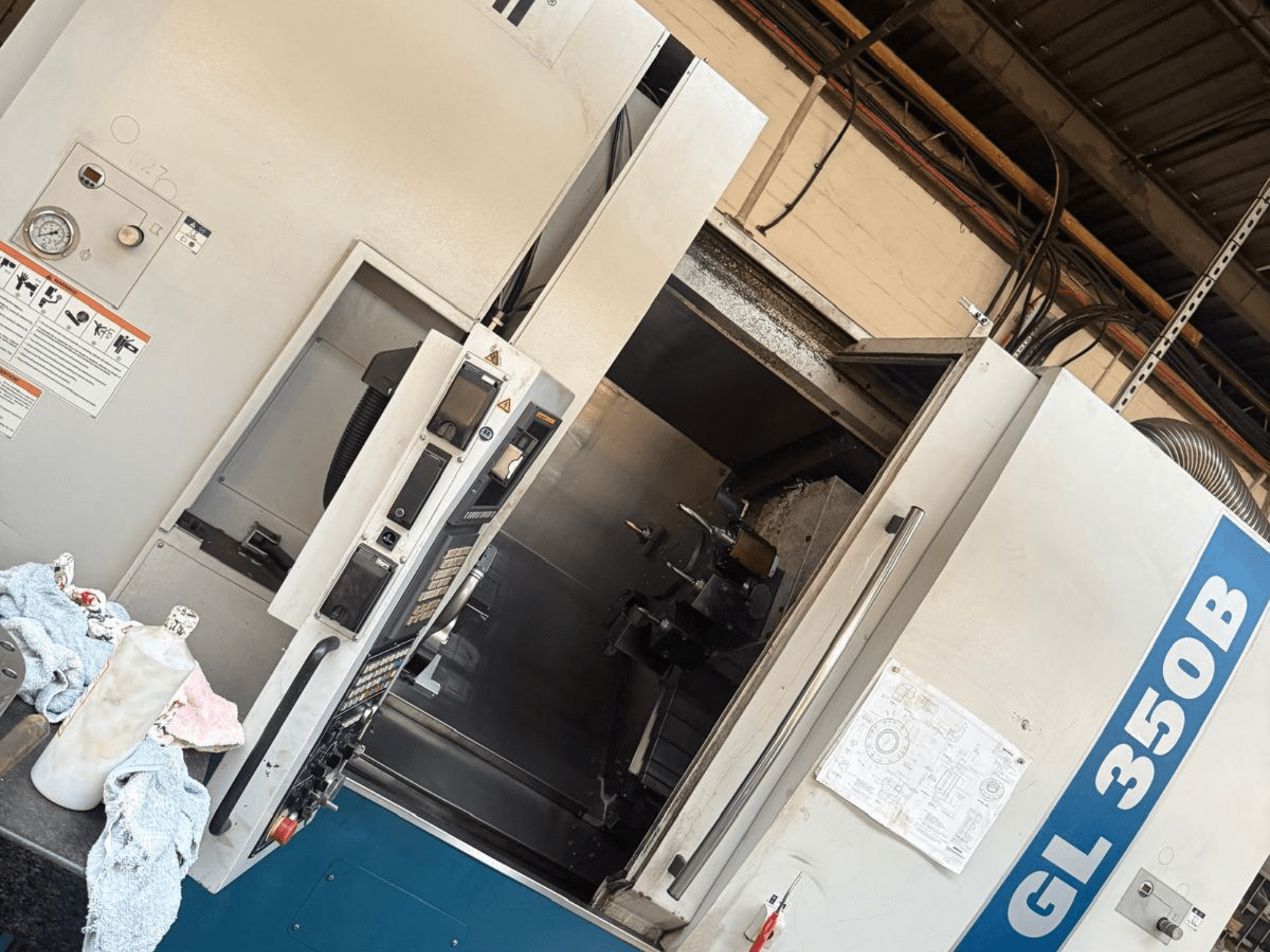 Vízszintes esztergagép Romi GL 350B, elölnézet, a kezelőpanellel és a nyitott ajtóval, amely a belső teret mutatja.