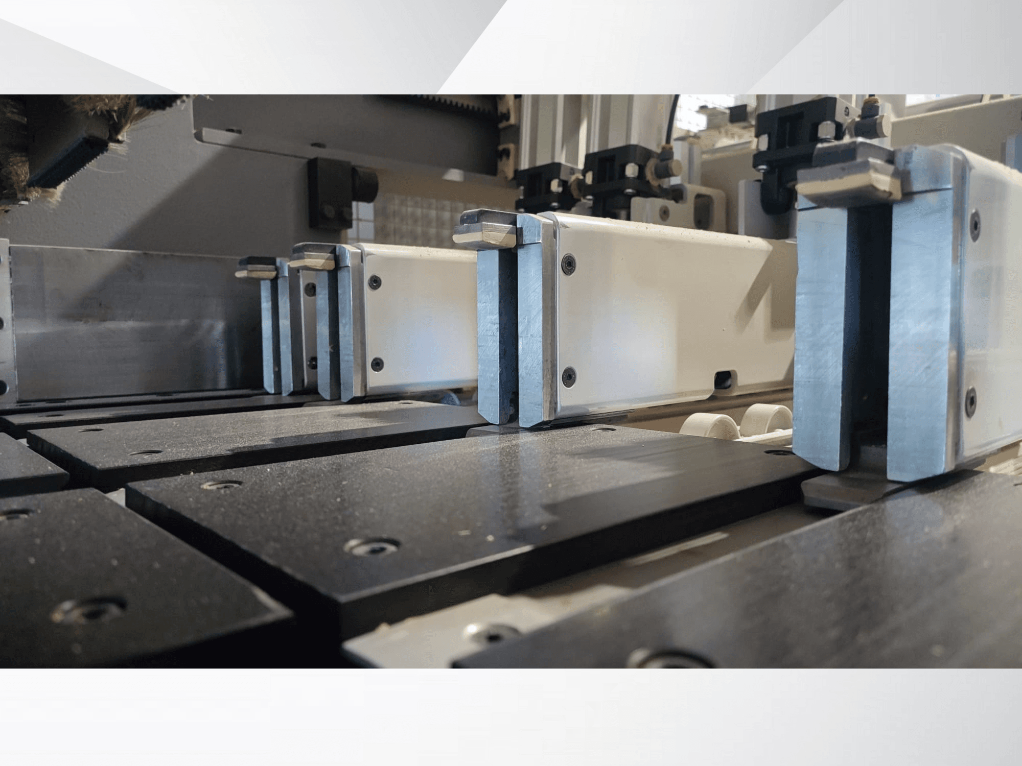 Közelkép egy precíziós gép fémpofákkal ellátott, fekete munkafelületekkel és látható vezetősínekkel ellátott szorítószerkezetéről.