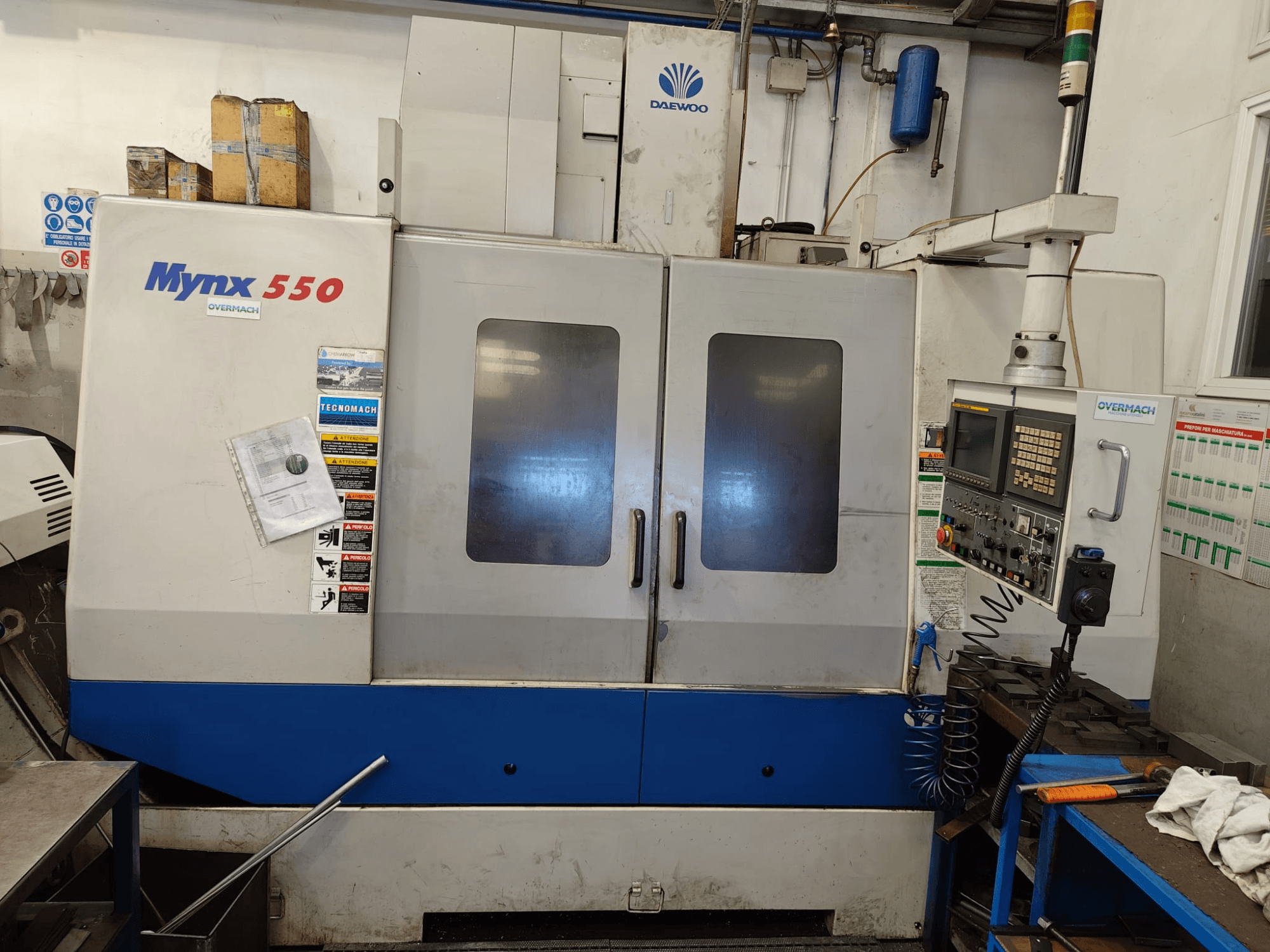 DAEWOO MYNX 550 függőleges megmunkáló központ, elölnézet, a vezérlőpanellel, két nagy ajtóval és biztonsági címkékkel.