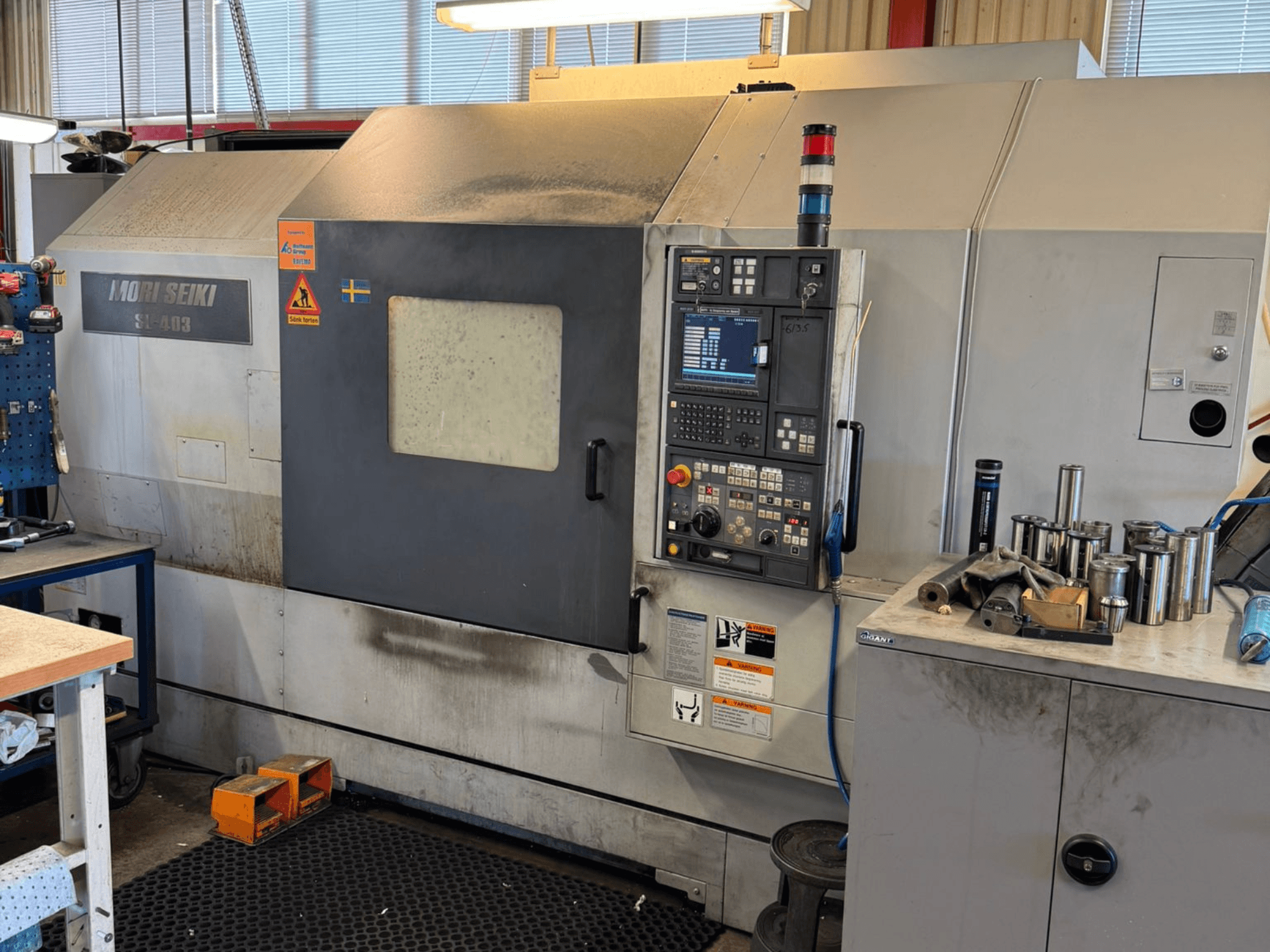 MORI SEIKI SL-403BMC/800 vízszintes esztergagép egy műhelyben, a vezérlőpanel és a közeli szerszámok, oldalnézet.