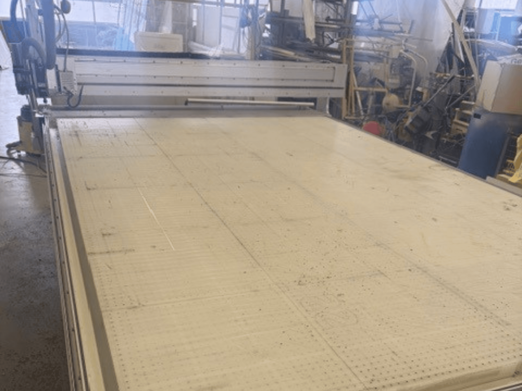 Nagyméretű, sík felületű vágógép, amelyen a keret és a vezetősín látható; szögből, műhelyben.