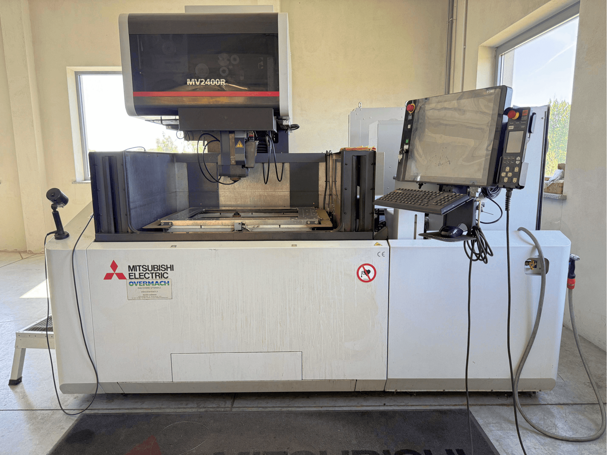 A Mitsubishi MV2400R huzalos szikraforgácsoló gép elölnézetben, a vezérlőpanellel, a munkaterülettel és a biztonsági jelzésekkel.