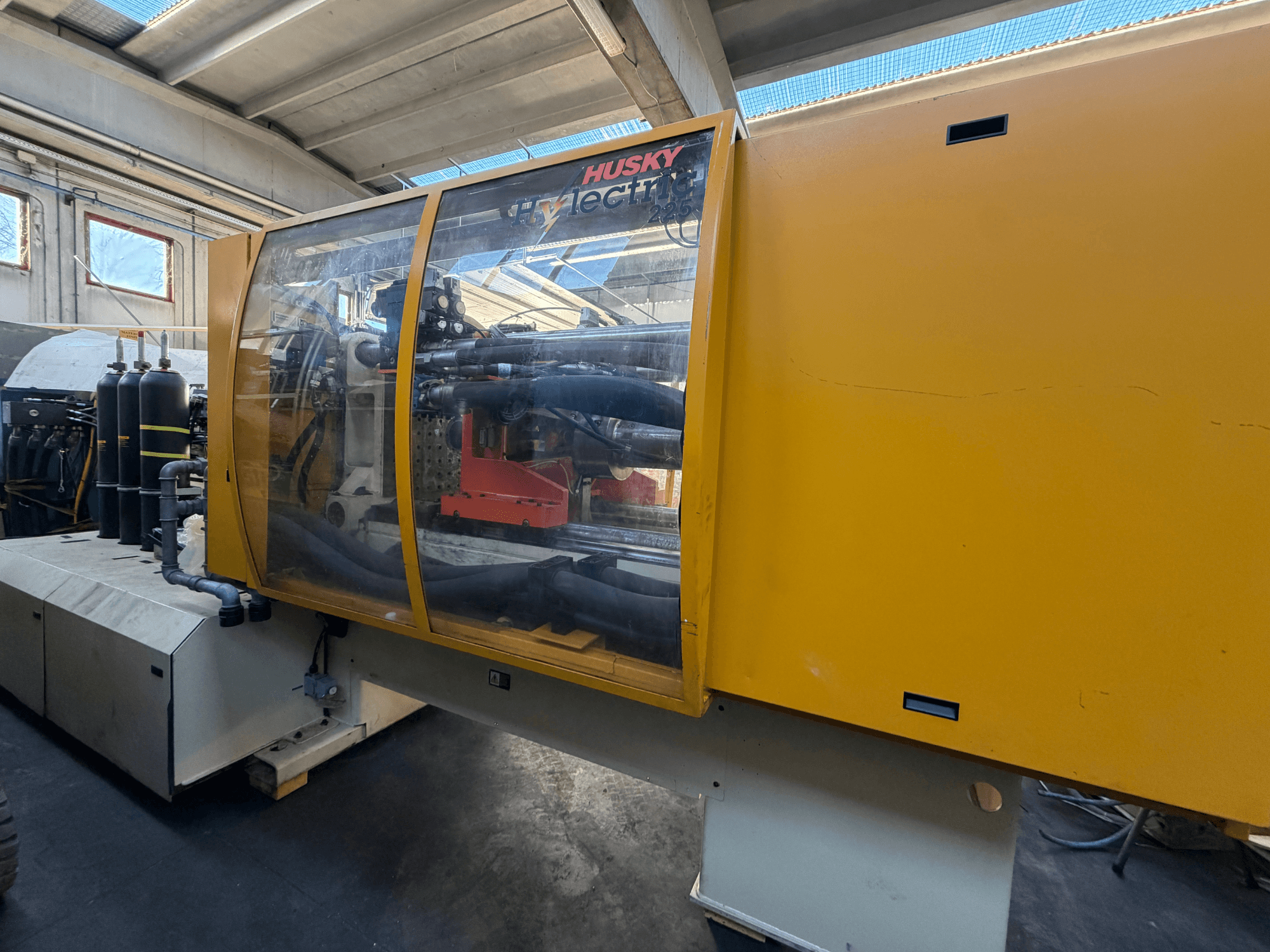 Husky HL225 RS65 elektromos fröccsöntőgép, elölnézetben, sárga burkolattal, látható vezérlőpanellel és hidraulikus alkatrészekkel.