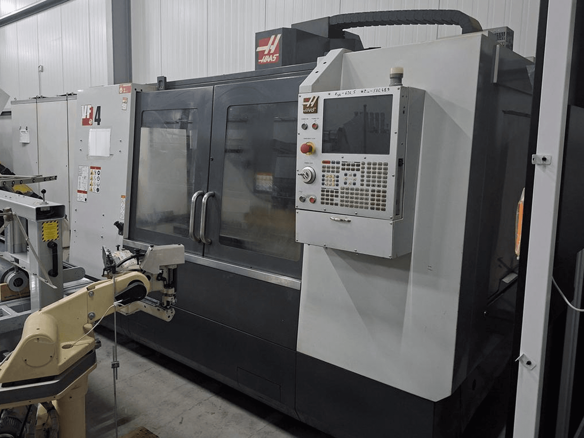 Haas VF-4 CNC marógép elölnézetben, numerikus vezérlőpanellel és robotkarral az automatizáláshoz.