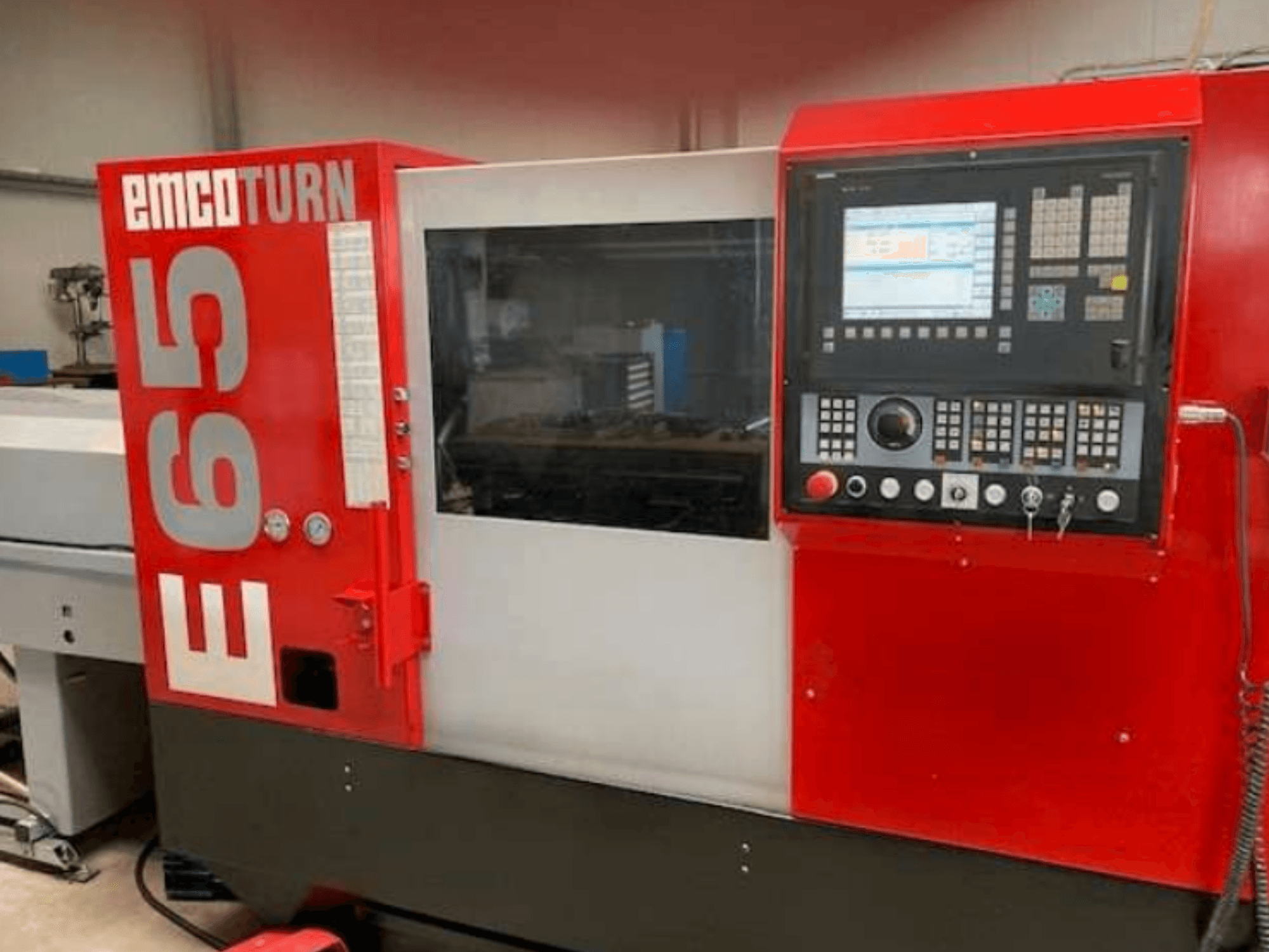 EMCO Turn E65 CNC eszterga, elölnézetben a vezérlőpanel, a nagy kijelző és az üveg mögötti munkaterület.