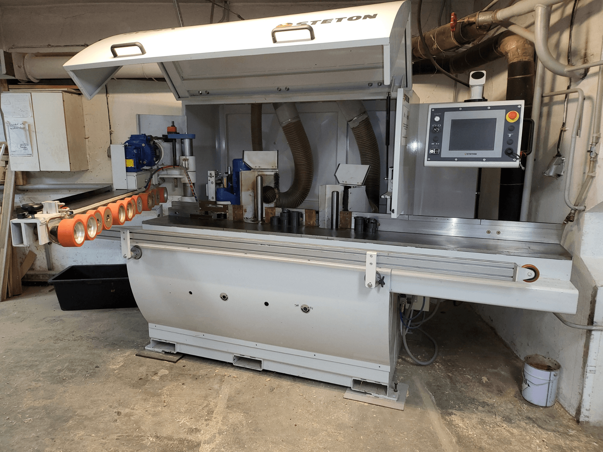 Egy Stetton famegmunkáló gép elülső nézete a vezérlőpanellel, az adagolócsövekkel és az asztalon lévő különböző fadarabokkal.