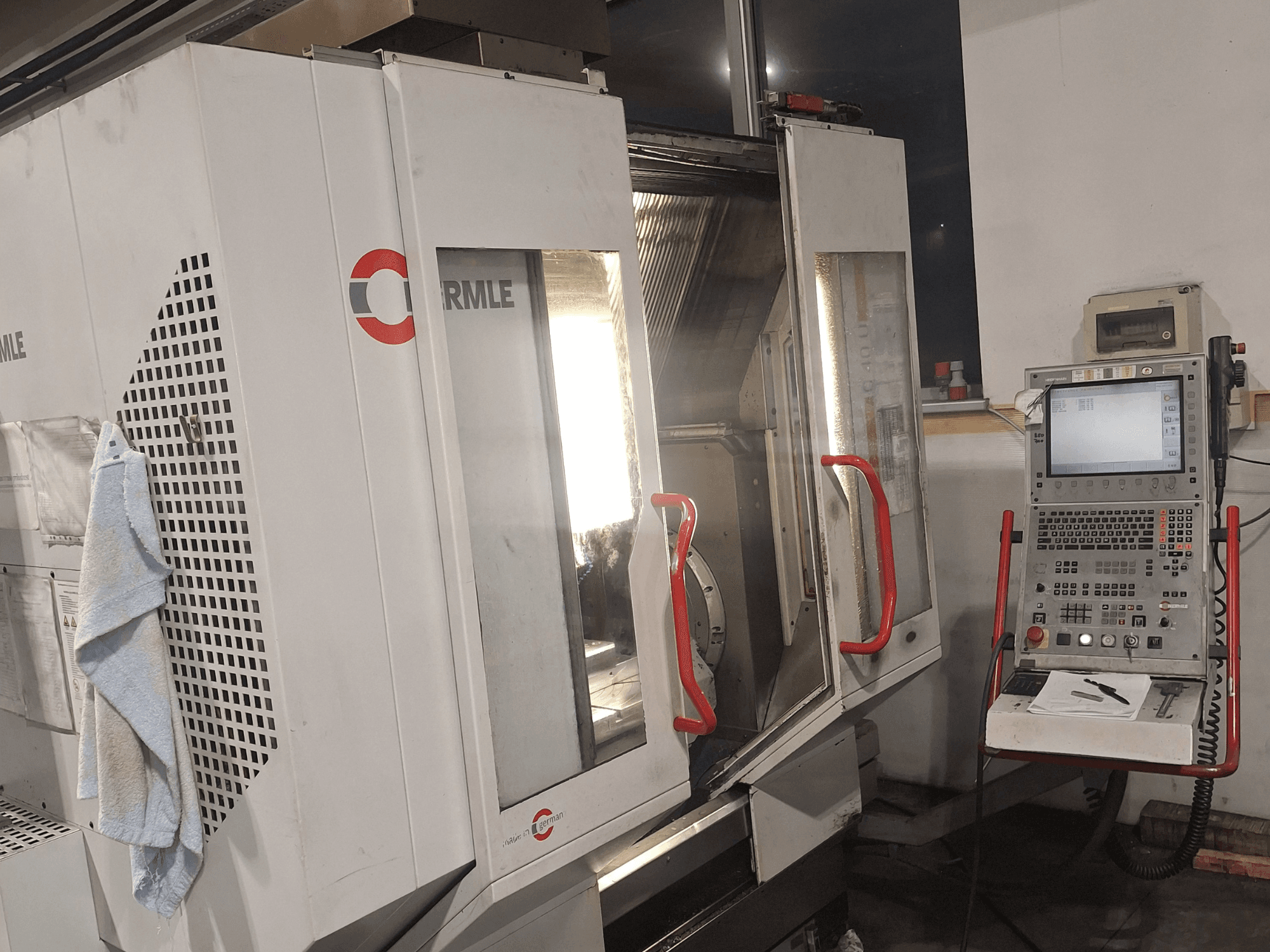 CNC-gép a Cormile márkától, elölnézetben a részben nyitott ajtók és a képernyővel és gombokkal ellátott vezérlőpanel.