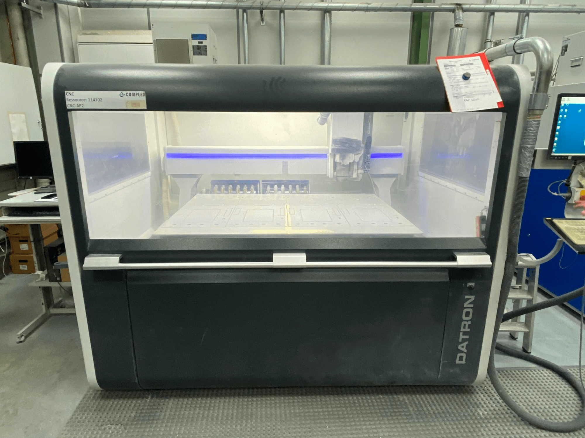 Egy Datron MLCube B függőleges megmunkálóközpont előlnézetben, látható kezelőszervekkel és munkaasztallal, műhelykörnyezetben.