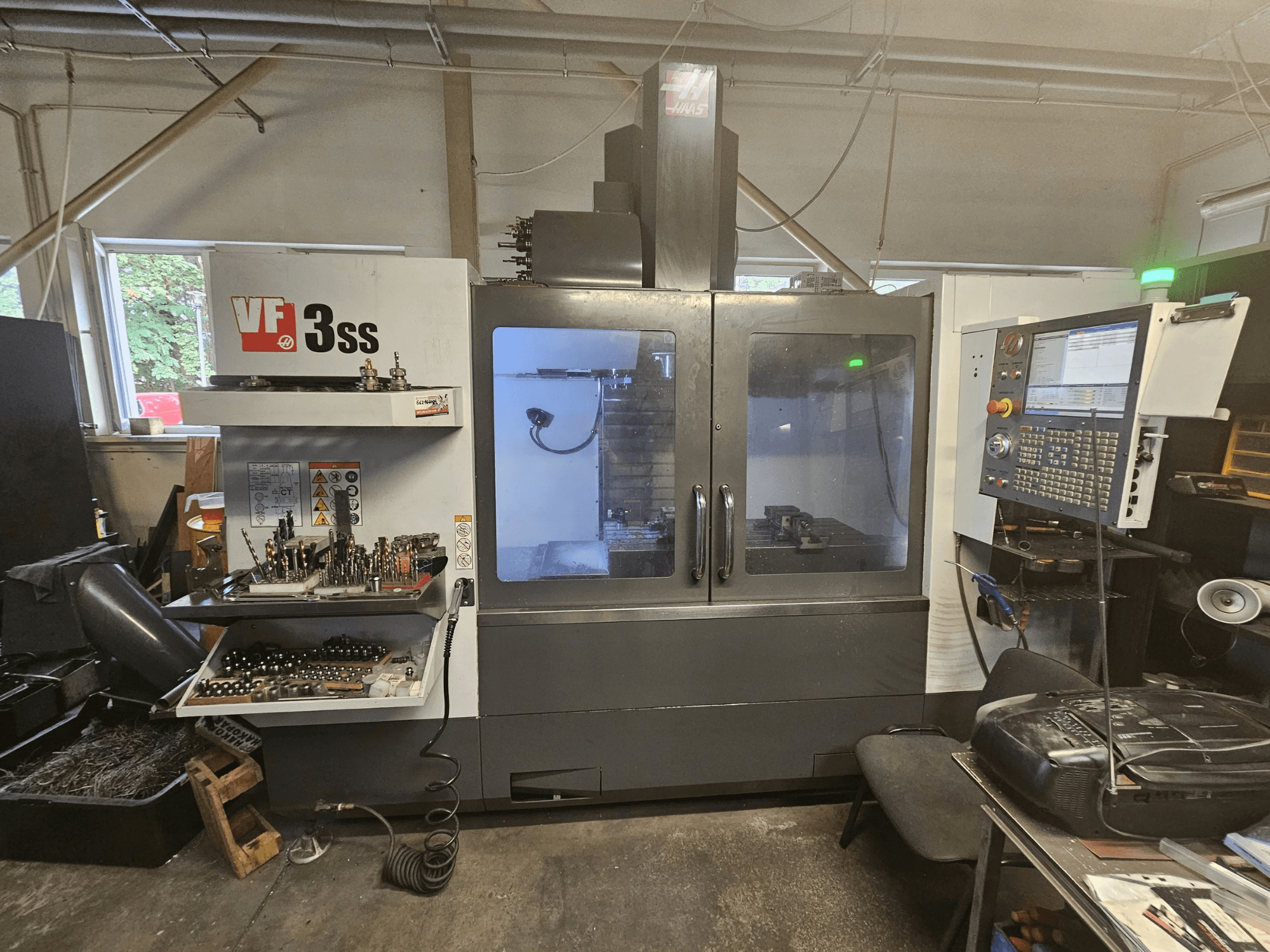 Haas VF-3SS függőleges megmunkáló központ egy műhelyben, elölnézetből, amelyen látható a vezérlőpanel és a szerszámtároló rekesz.