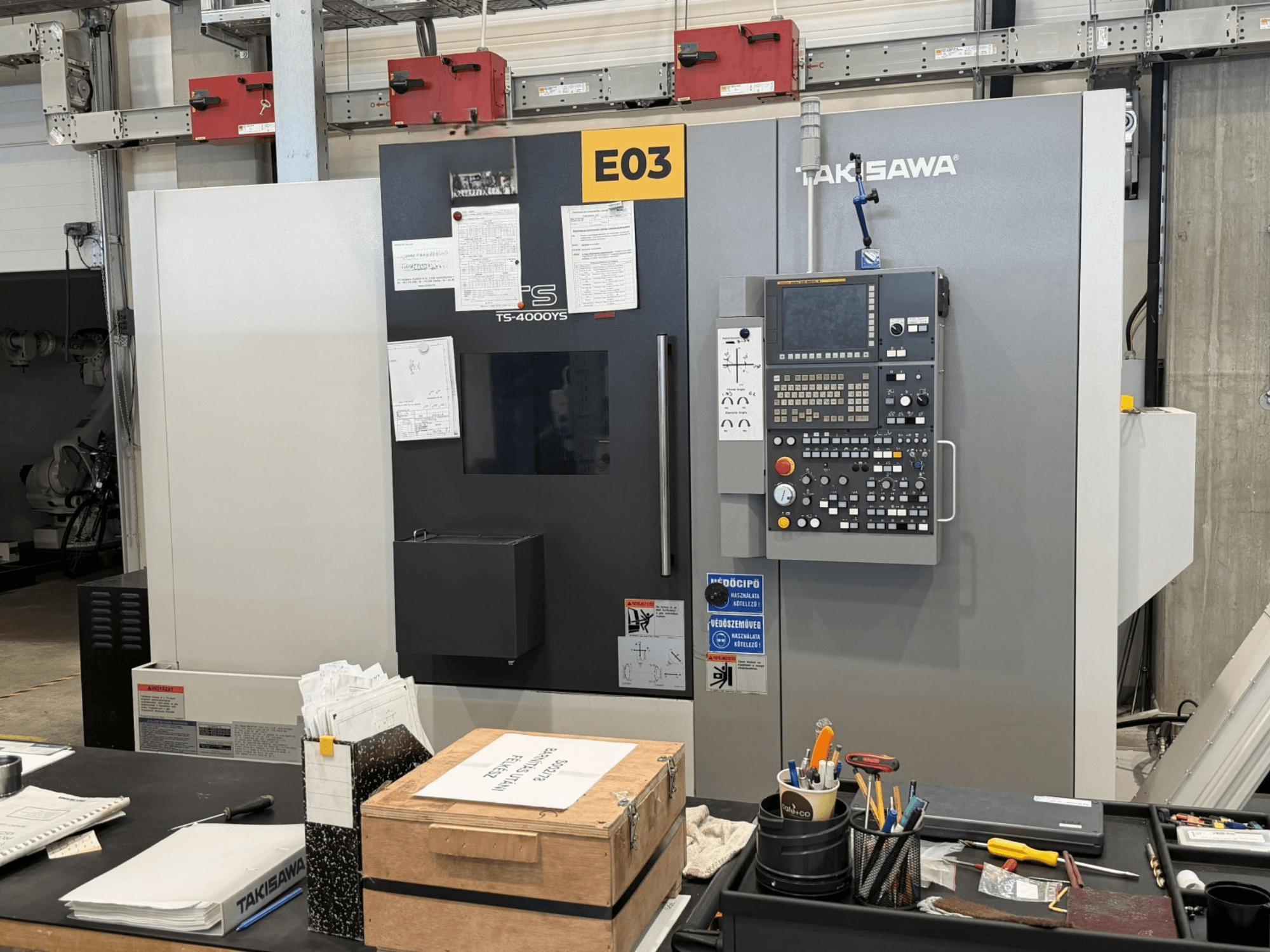 A Takisawa TS-4000YS eszterga-marógép elölről nézve, oldalán a vezérlőpanellel és a dokumentumokkal.