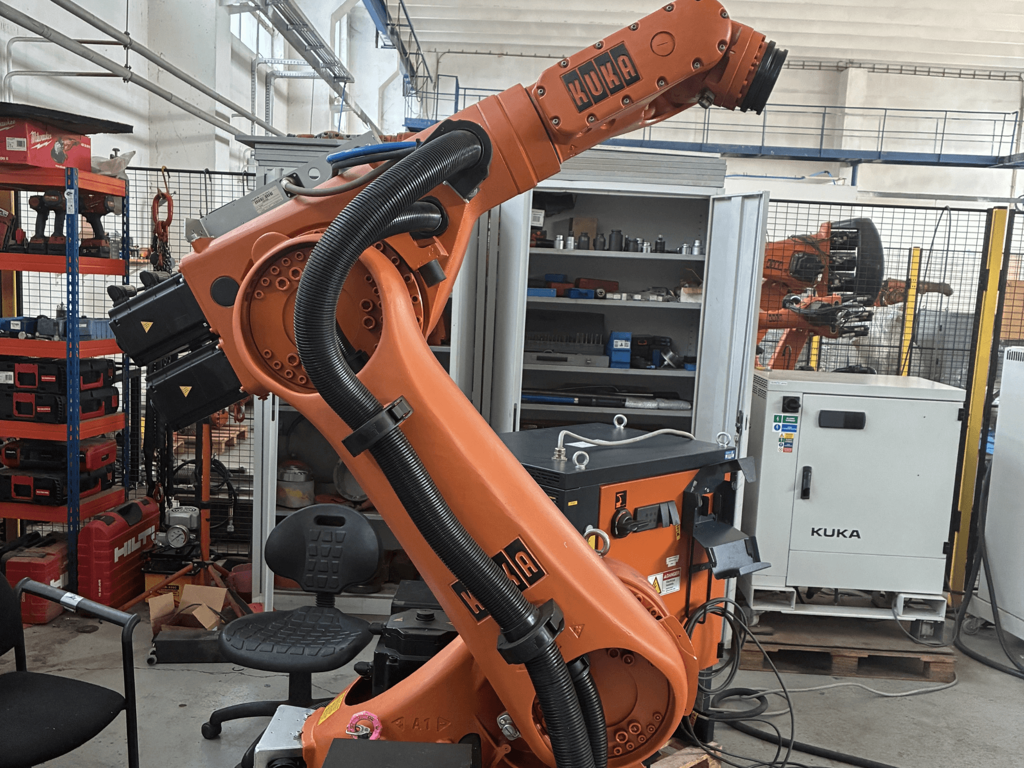 KUKA KR30-3 robotkar ipari környezetben, oldalnézetben a kábelek és kezelőszervek, háttérben szerszámok és polcok.