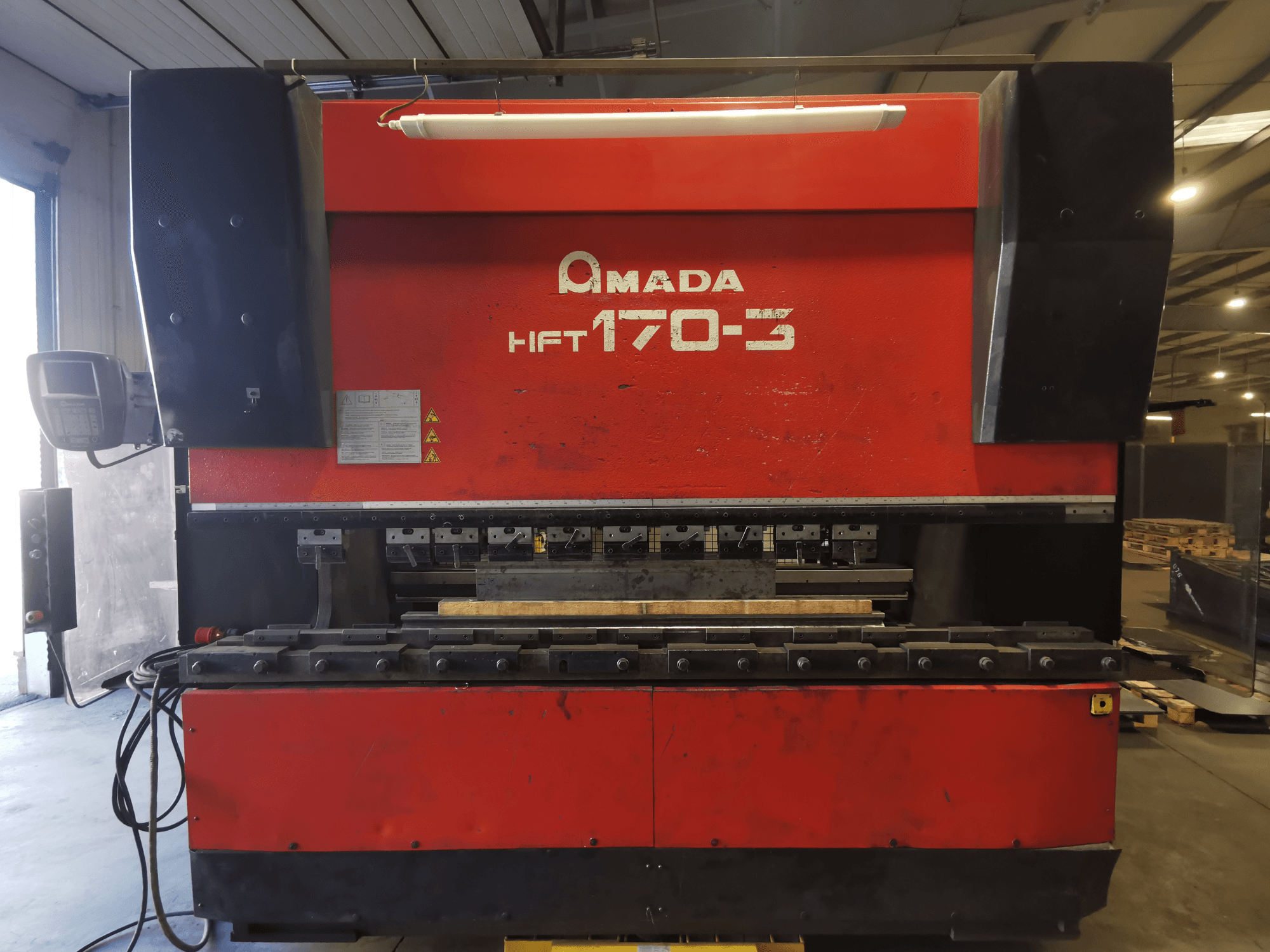 Piros Amada HFT 170-3 présfék elölről nézve, a vezérlőpanel, a hajlítószerszámok és a munkafelület látható.