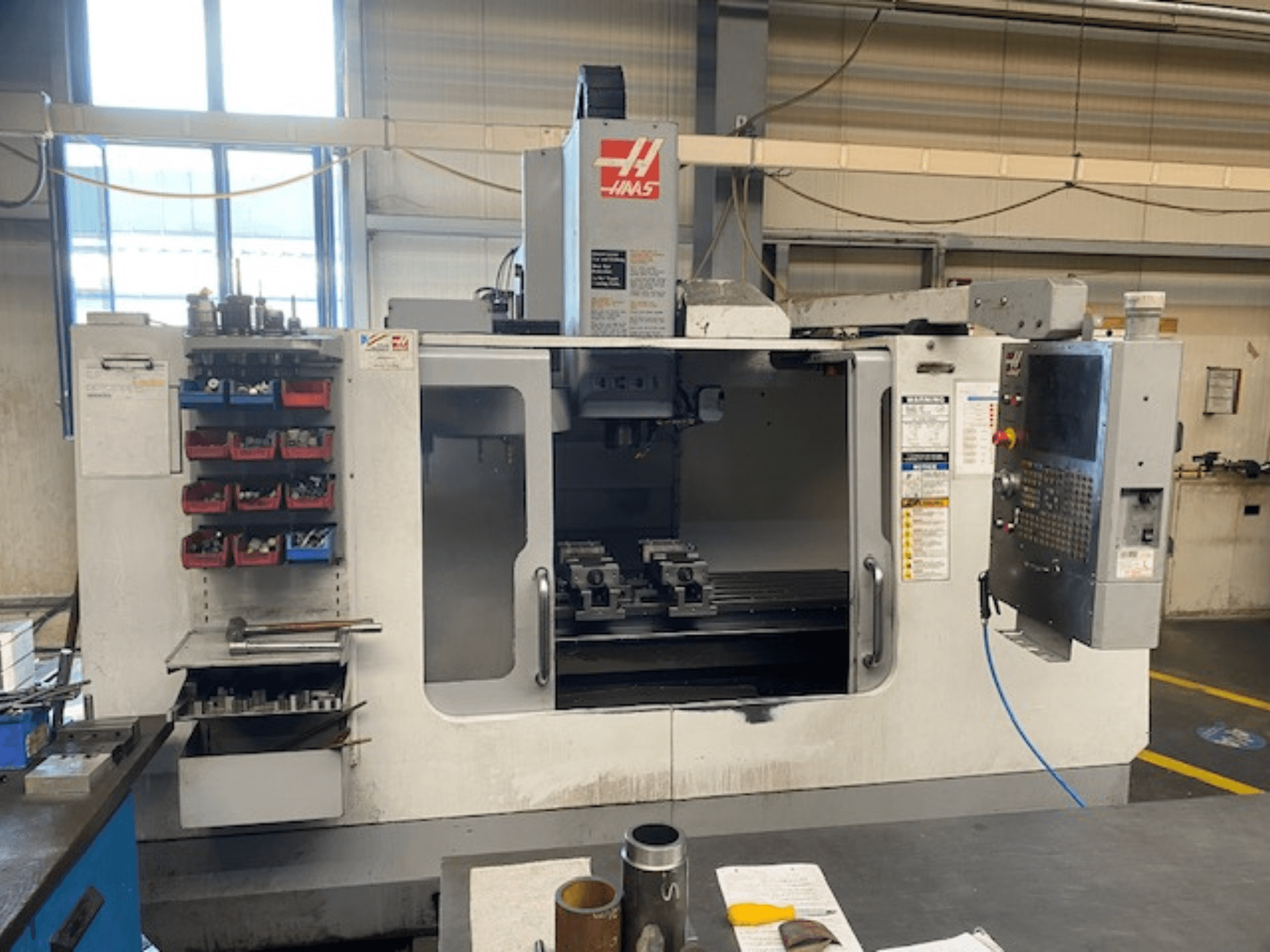 Haas CNC marógép előlnézetben, VF-2 modell, szerszámtároló, vezérlőpanel és munkaterület szerszámok láthatóak.
