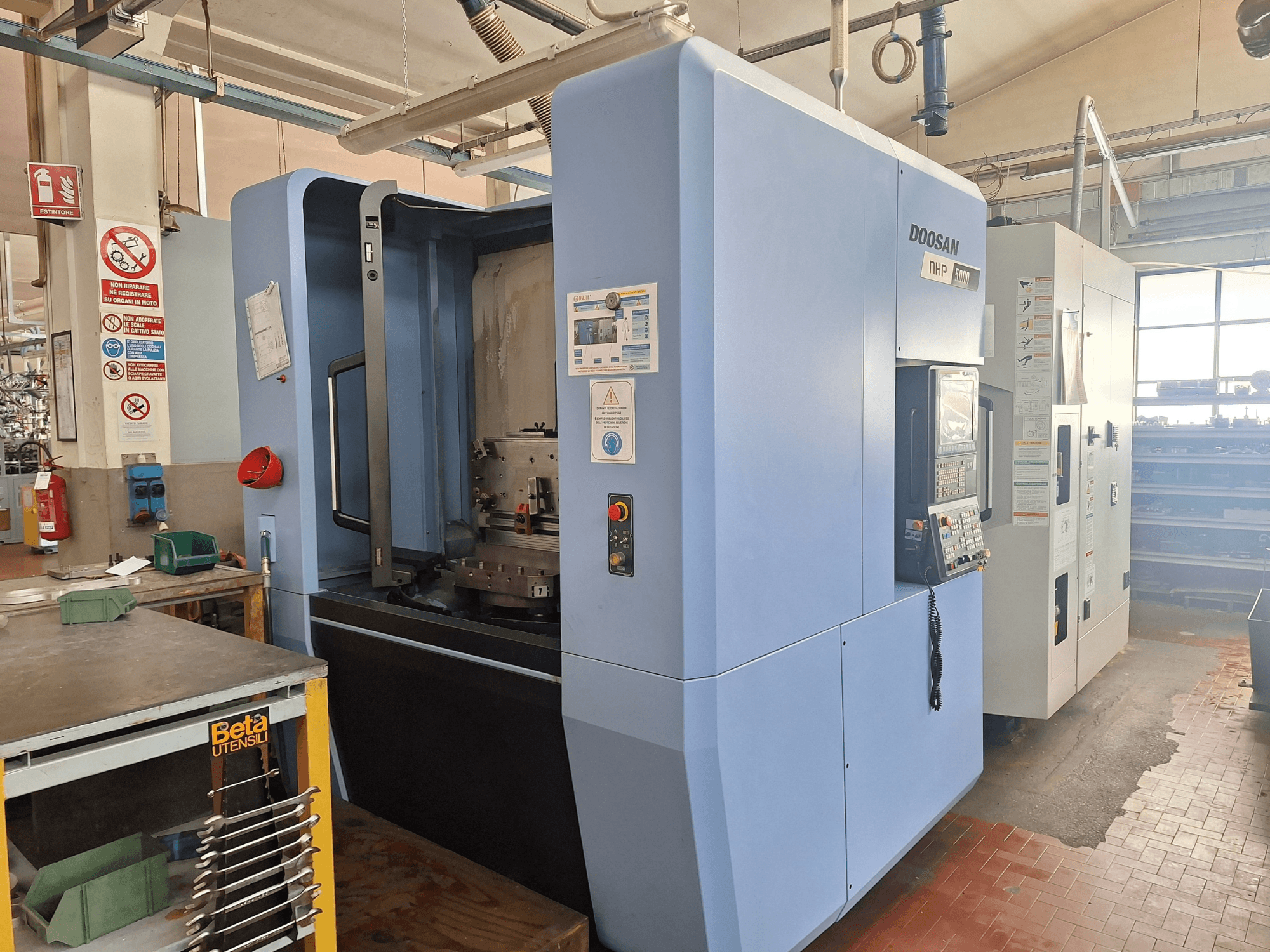 DOOSAN NHP 5000 vízszintes megmunkálóközpont egy műhelyben, oldalnézetben a vezérlőpanel és a megmunkálóterület.