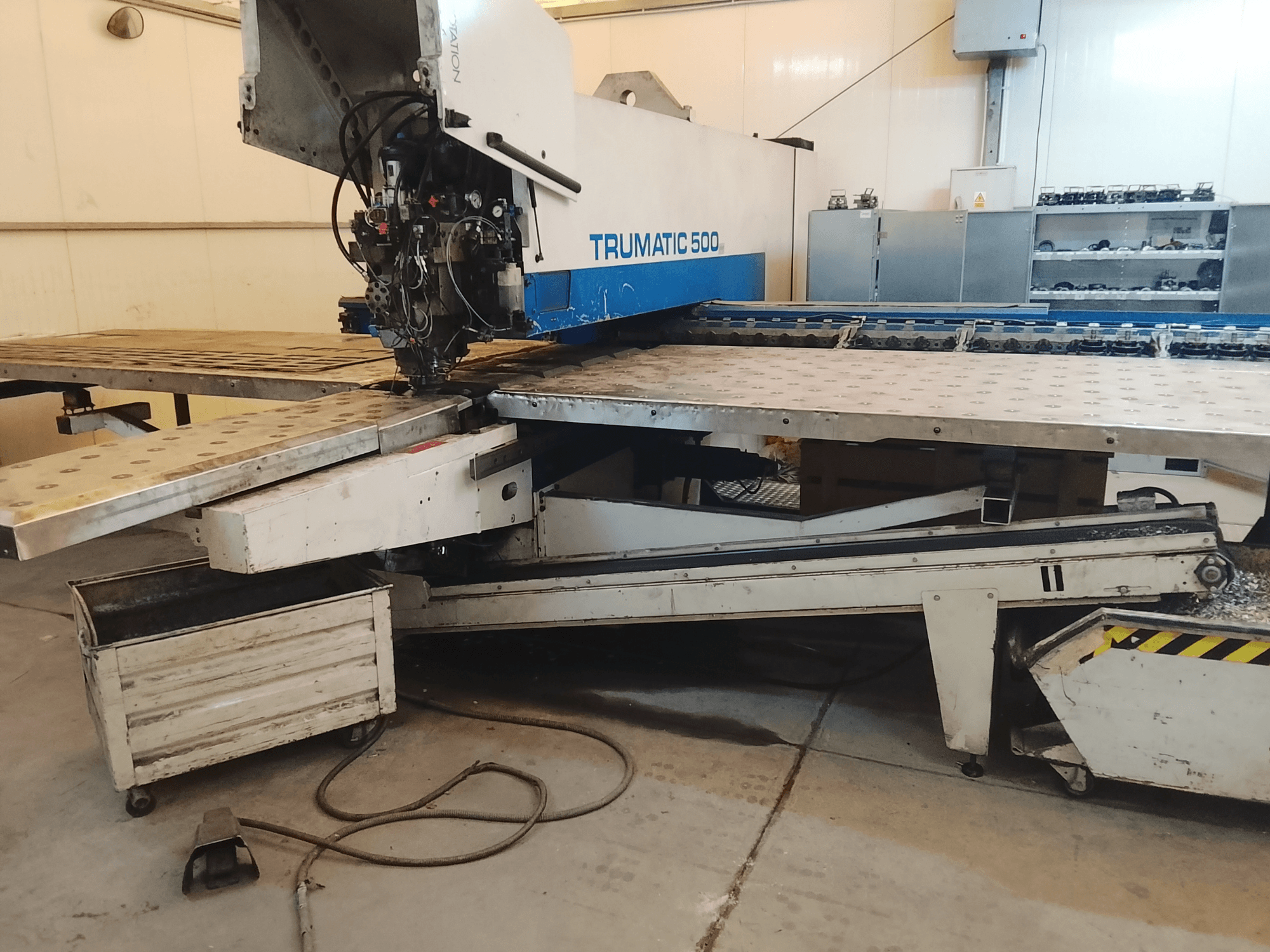 TRUMATIC 500 CNC-gép egy műhelyben, oldalnézetben a vágófej és az előfúrt lyukakkal ellátott fém munkaasztal.