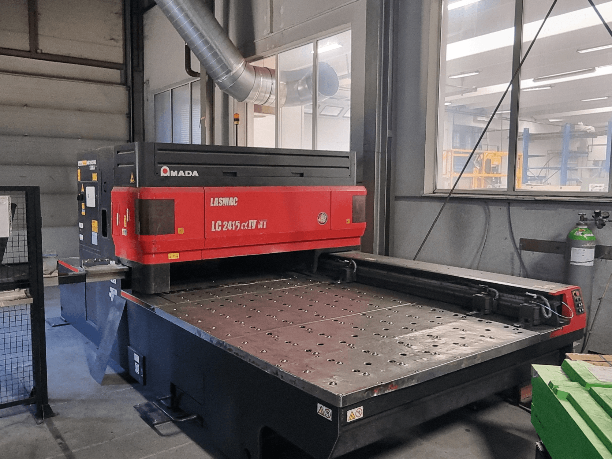 Amada LASMAC LC 2415 αⅡ NT lézervágógép piros-fekete színben, elölnézetben, motoros vágóasztallal és precíziós vezérléssel.