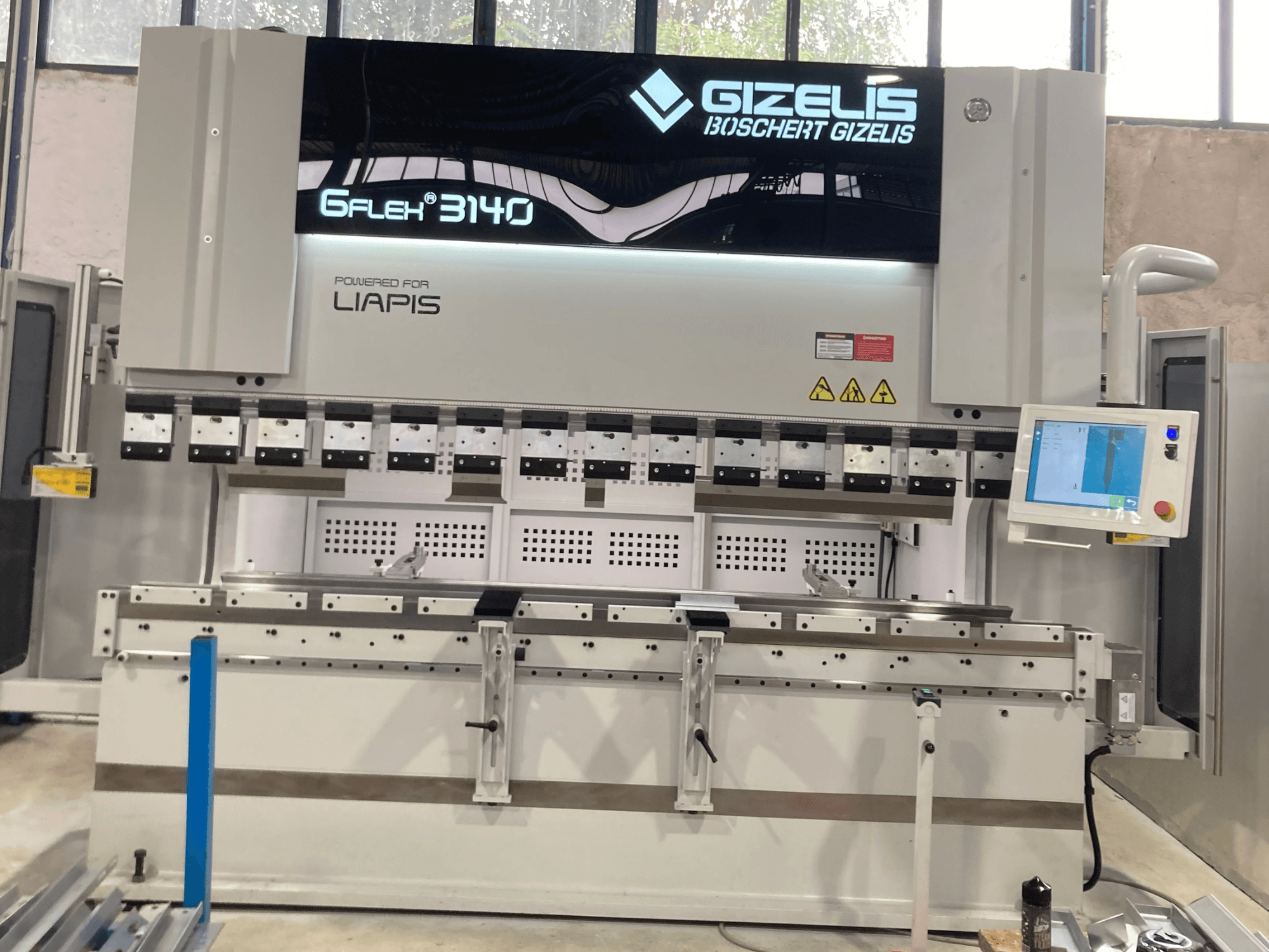 GIZELIS G-FLEX 3140 hidraulikus prés elölnézetben, vezérlőképernyővel, több hajlítószerszámmal és biztonsági címkékkel.