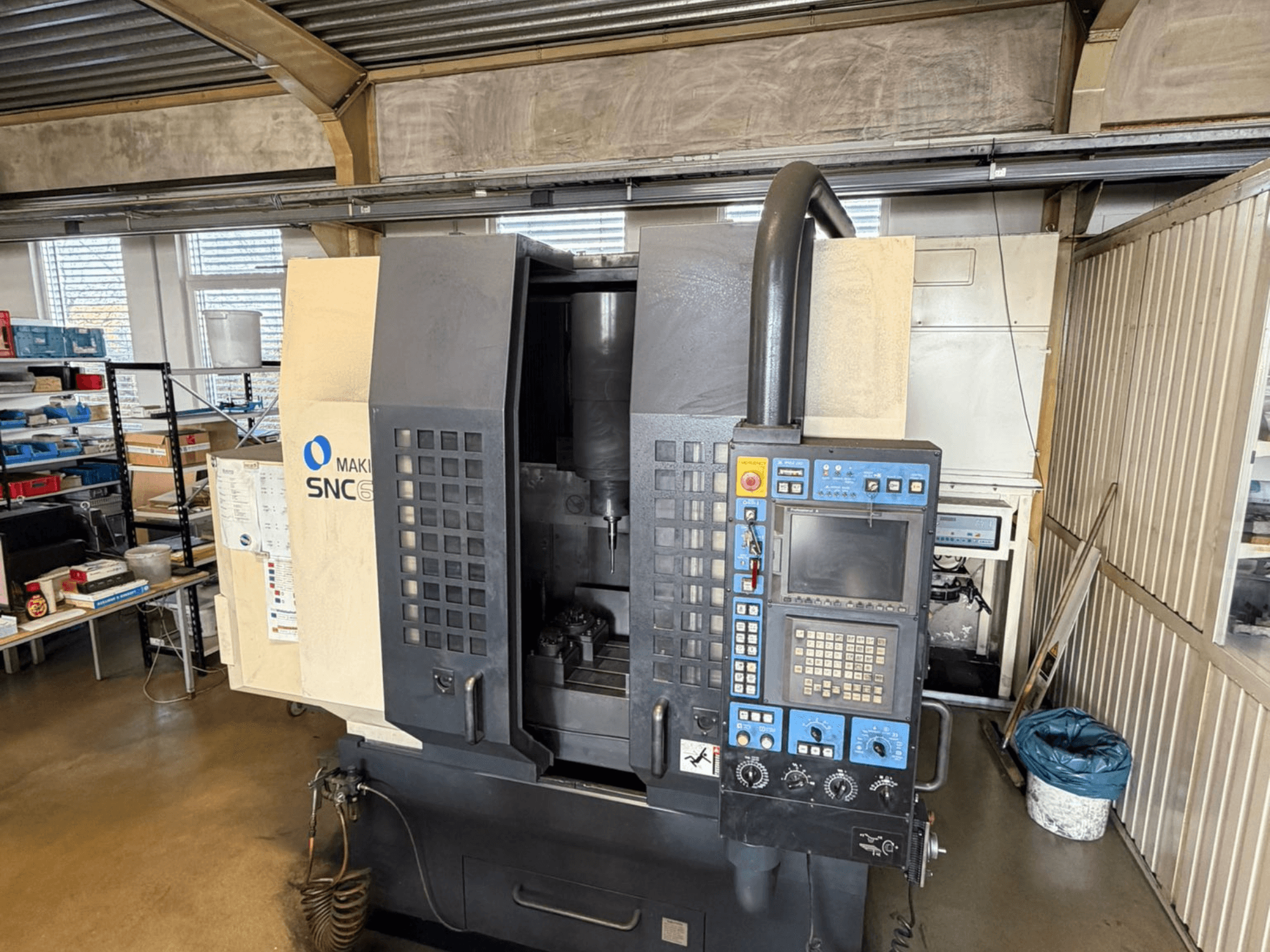 Makino SNC 64-A15 függőleges megmunkálóközpont elölnézetben, a vezérlőpanel, a megmunkálási terület és az ipari munkaterület bemutatásával.
