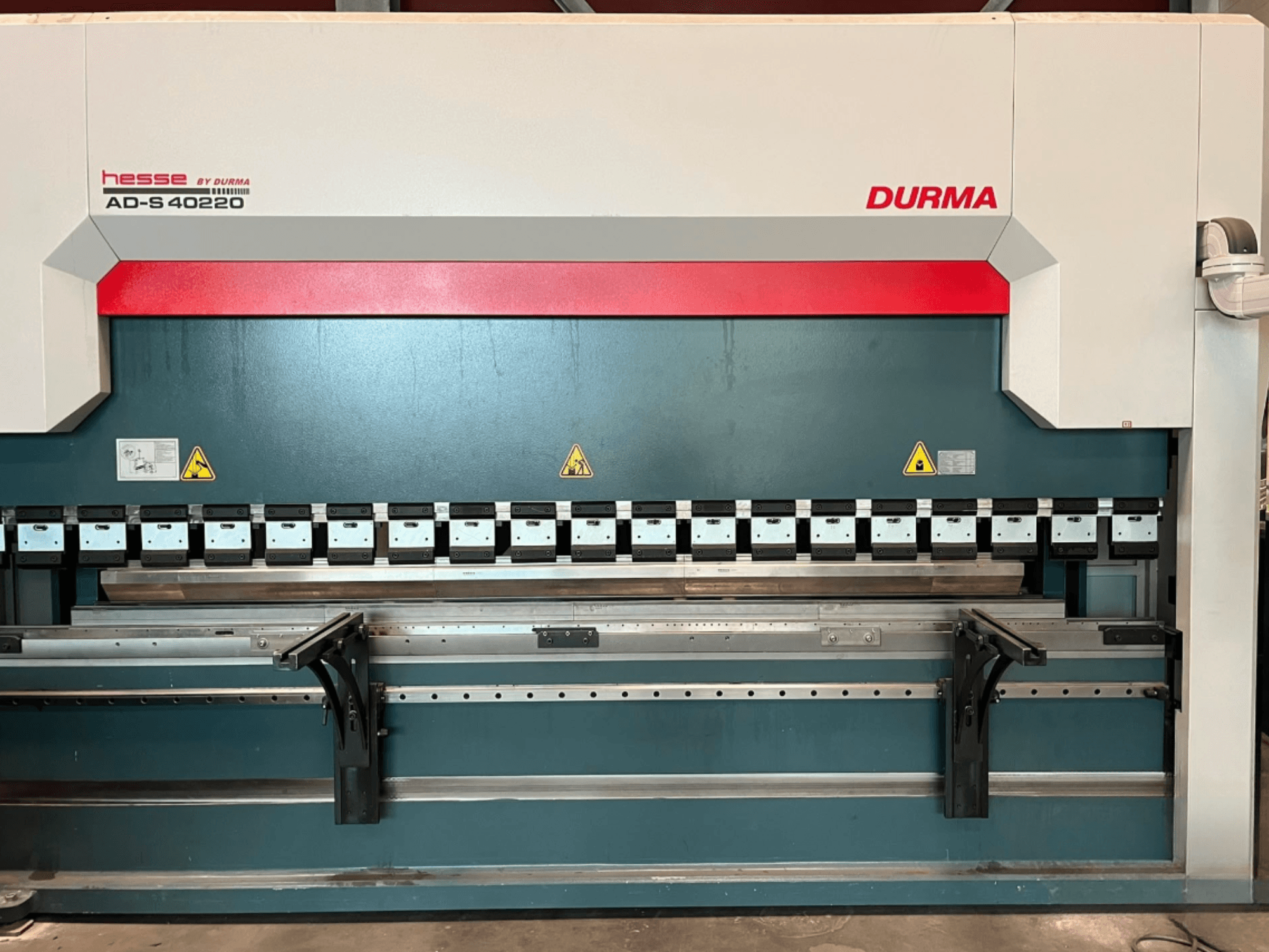 A Durma AD-S 40220 hajlítógép elölnézetből, többféle hajlítószerszámmal és biztonsági címkékkel ellátva.