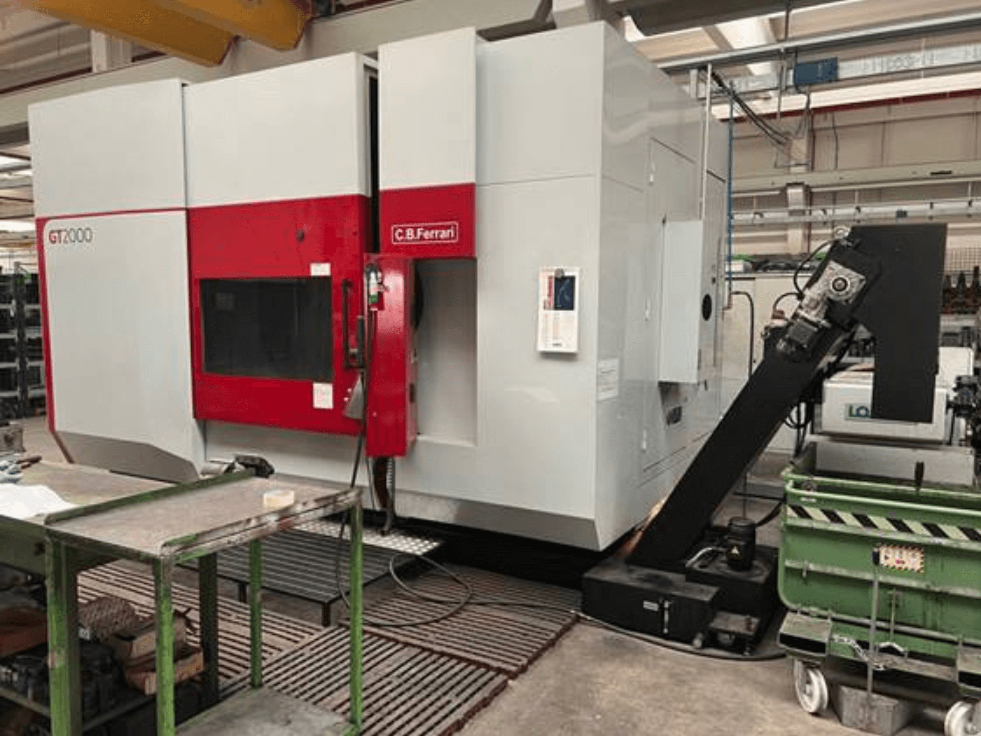 C.B. Ferrari GT2000 marógép elölnézetben, robotkarral és ipari munkaterülettel, zöld kocsival.