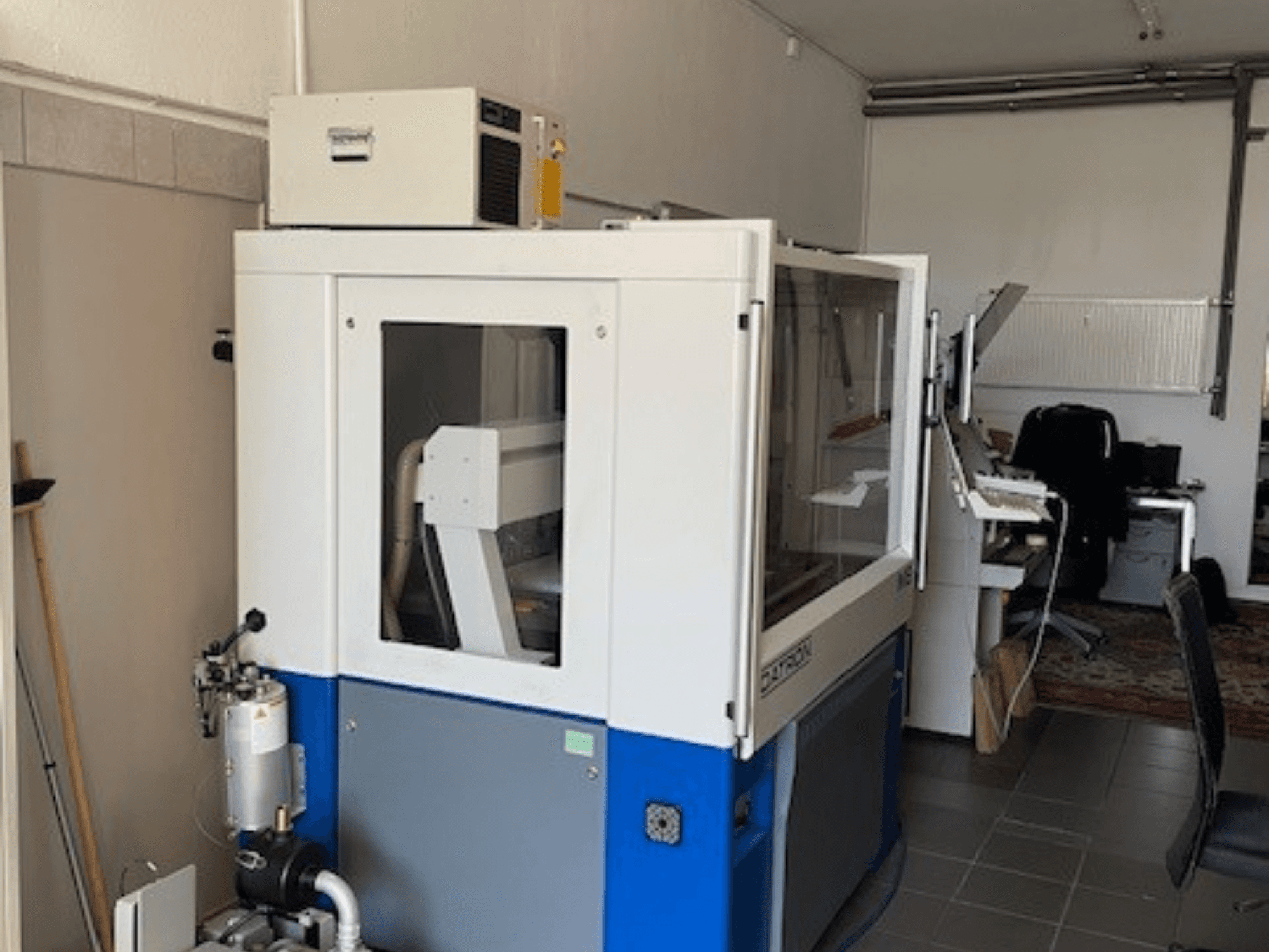 Kék-fehér ipari gép átlátszó panelekkel, elölnézetben, a vezérléshez való hozzáféréssel és a látható szellőztetőegységgel.