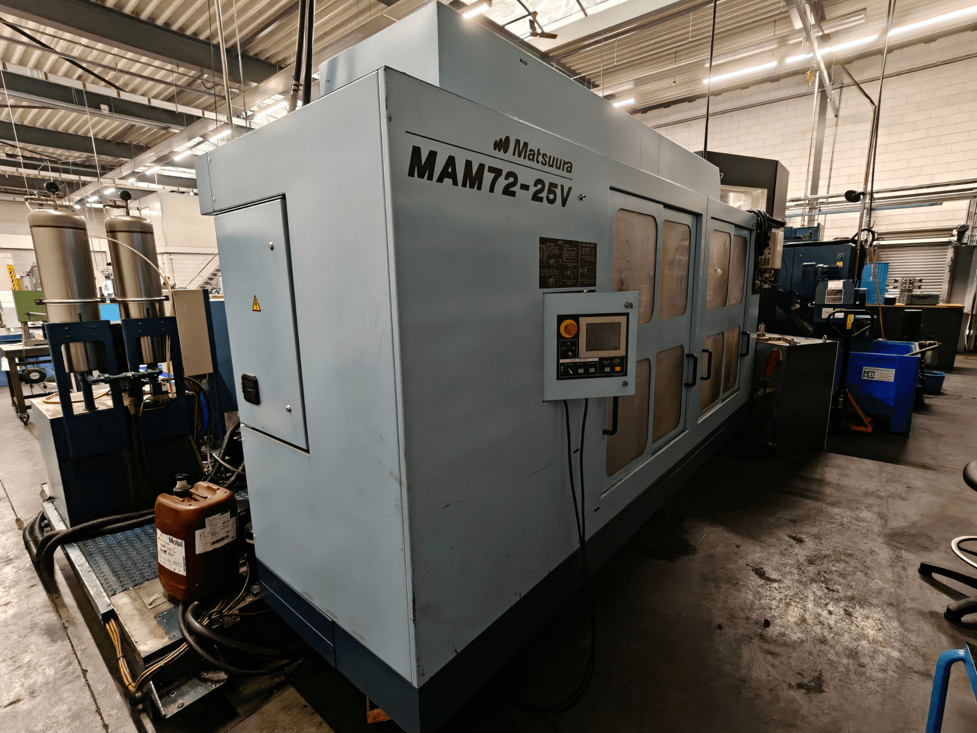 Matsuura MAM72-25V CNC-gép, oldalnézet, vezérlőpanel, kettős hűtőfolyadék-tartály és munkaterület ipari környezetben.