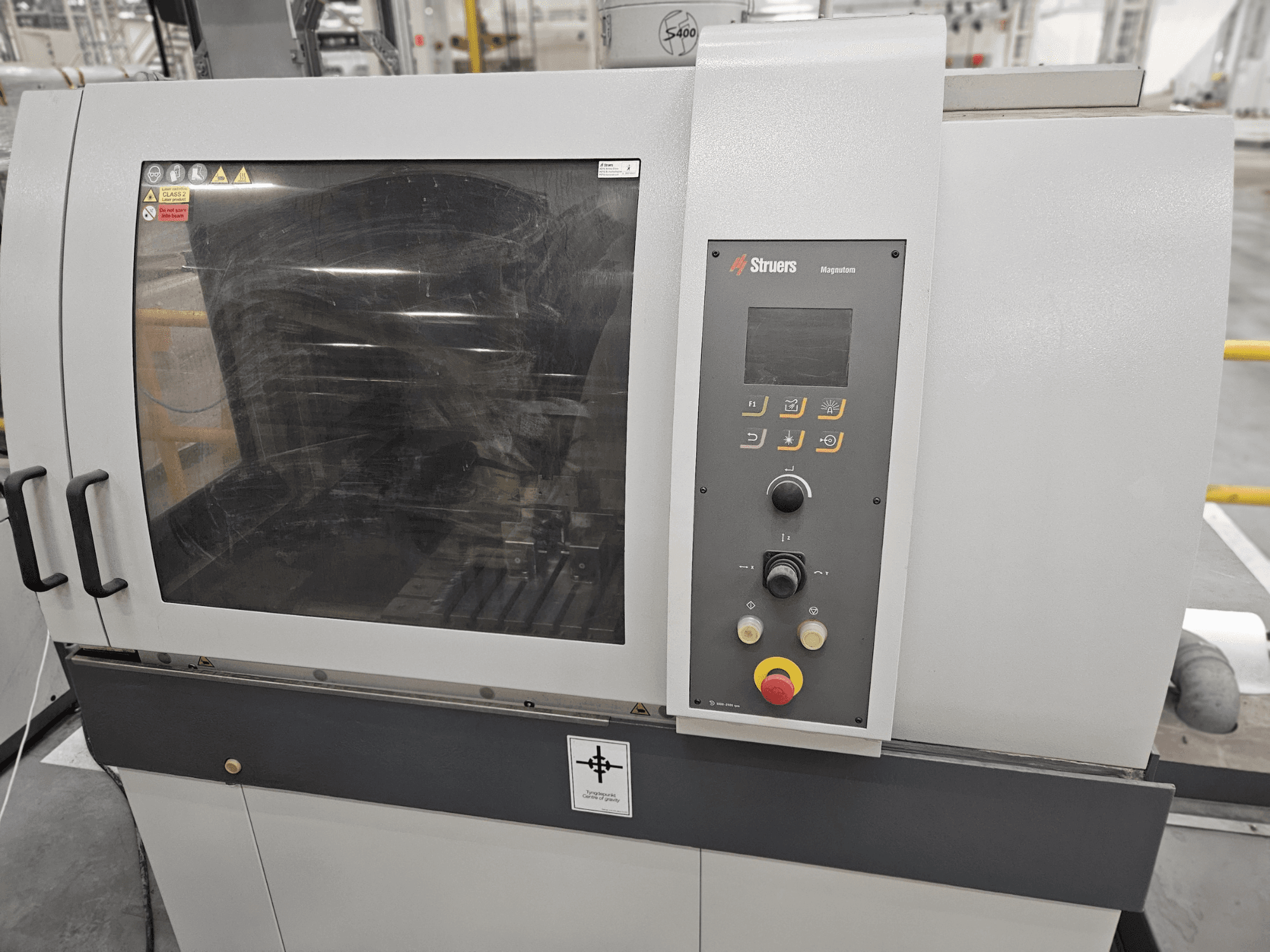 Struers Magpentor gép előlapja a kezelőpanellel, gombokkal és egy nagy ablakkal. Műszaki címkék láthatóak.