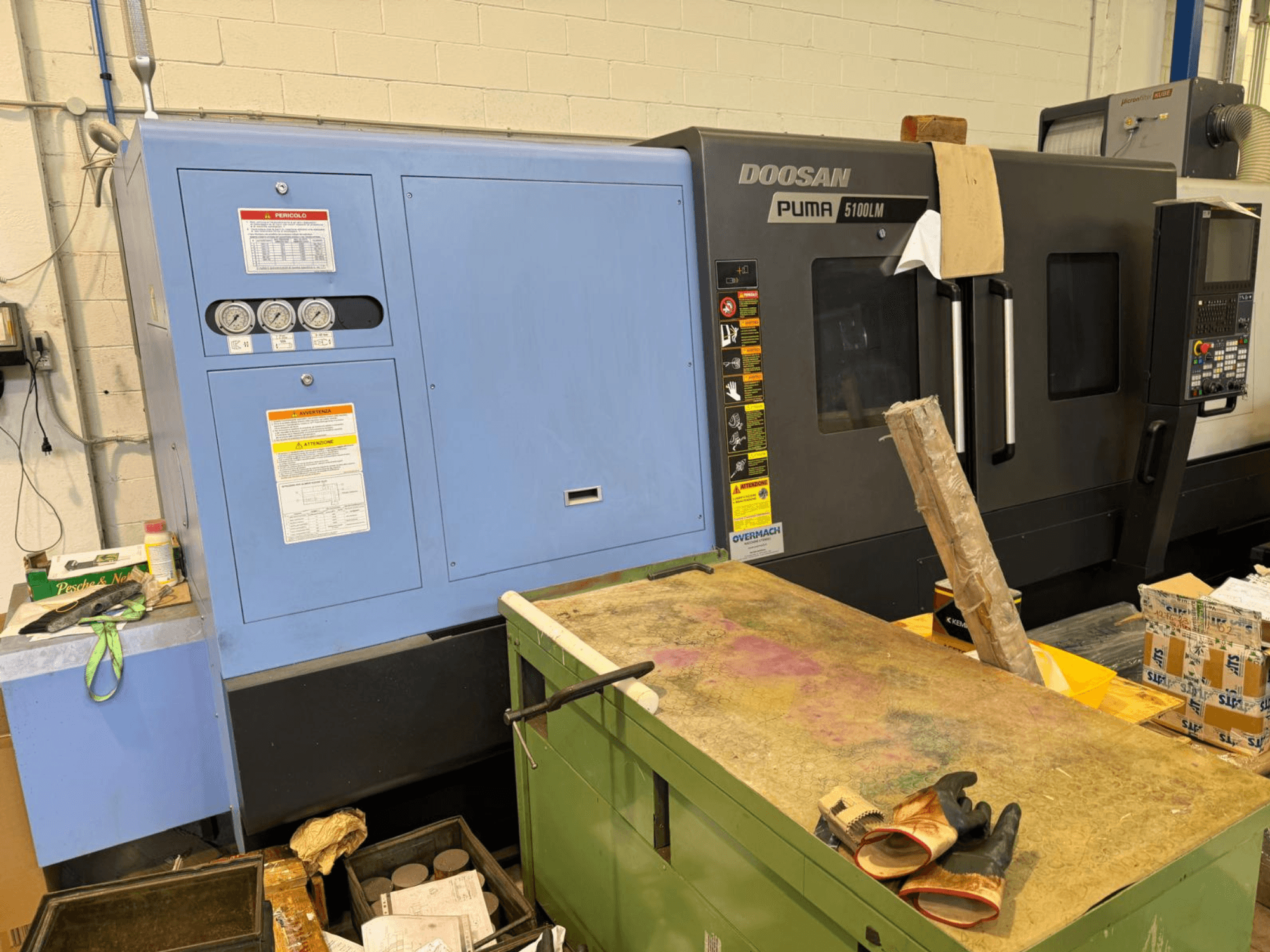 Doosan Puma 5100LM CNC gép és vezérlőpanel, oldalnézet. A kék vezérlőegységen látható műszerek és figyelmeztető feliratok.