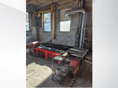 Vörös CNC plazmavágóasztal vezérlőpanellel és fém kipufogócsatornával, oldalról nézve egy jól megvilágított műhelyben.