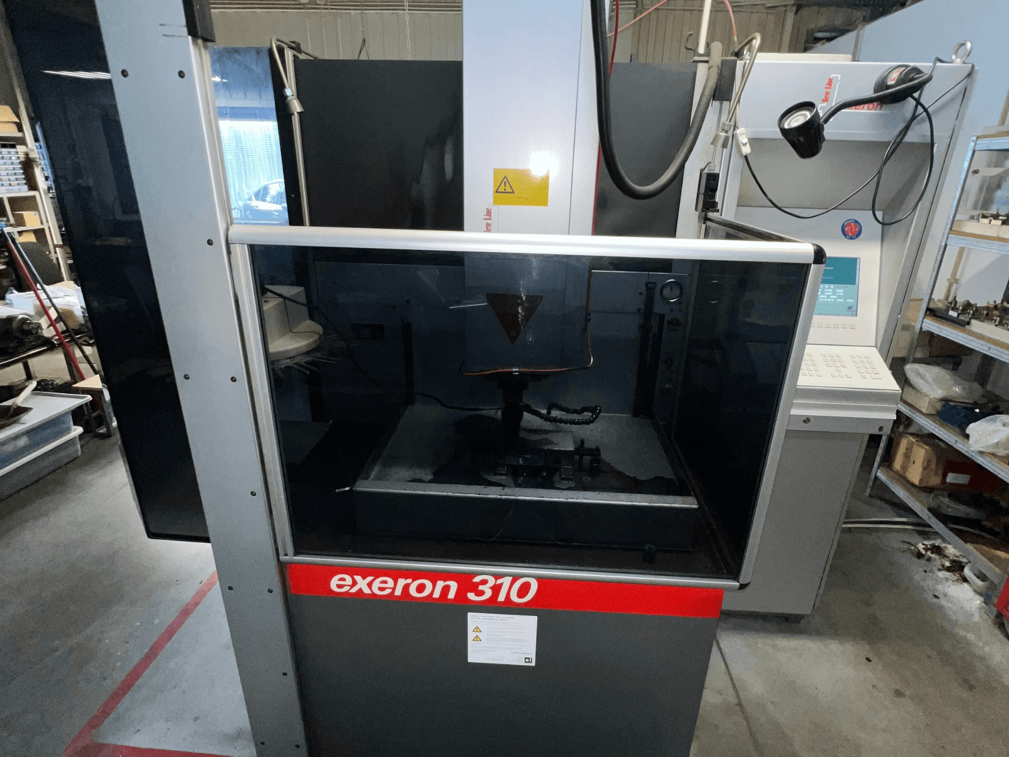 Egy Exeron 310-es gép elülső nézete, amely az üvegkamrát és a vezérlőpanelt mutatja a munkaállomás polcai mellett.