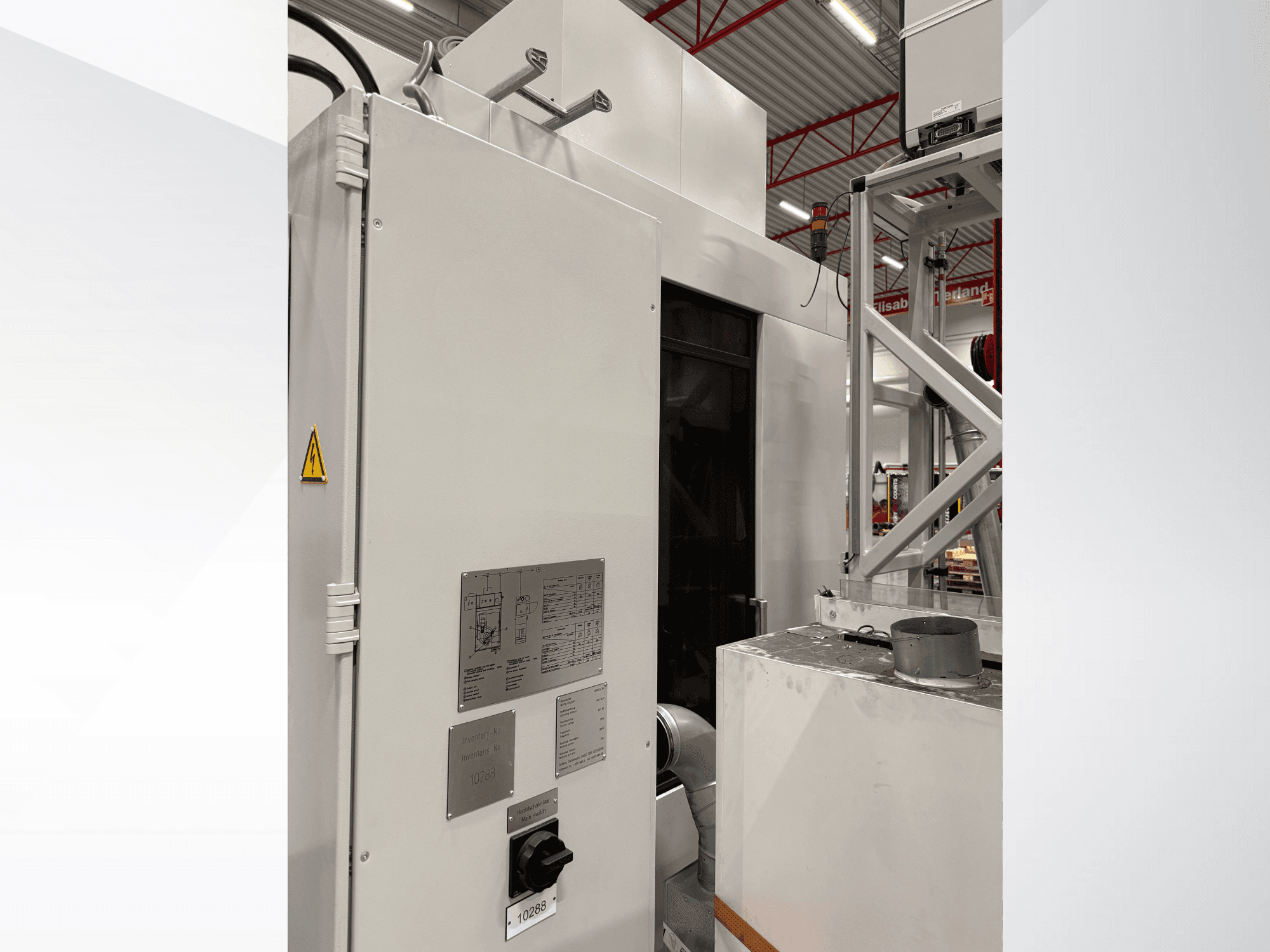 Egy fehér ipari gép oldalnézetben, vezérlőpanellel és figyelmeztető címkével, egy automatizált rendszer részeként.