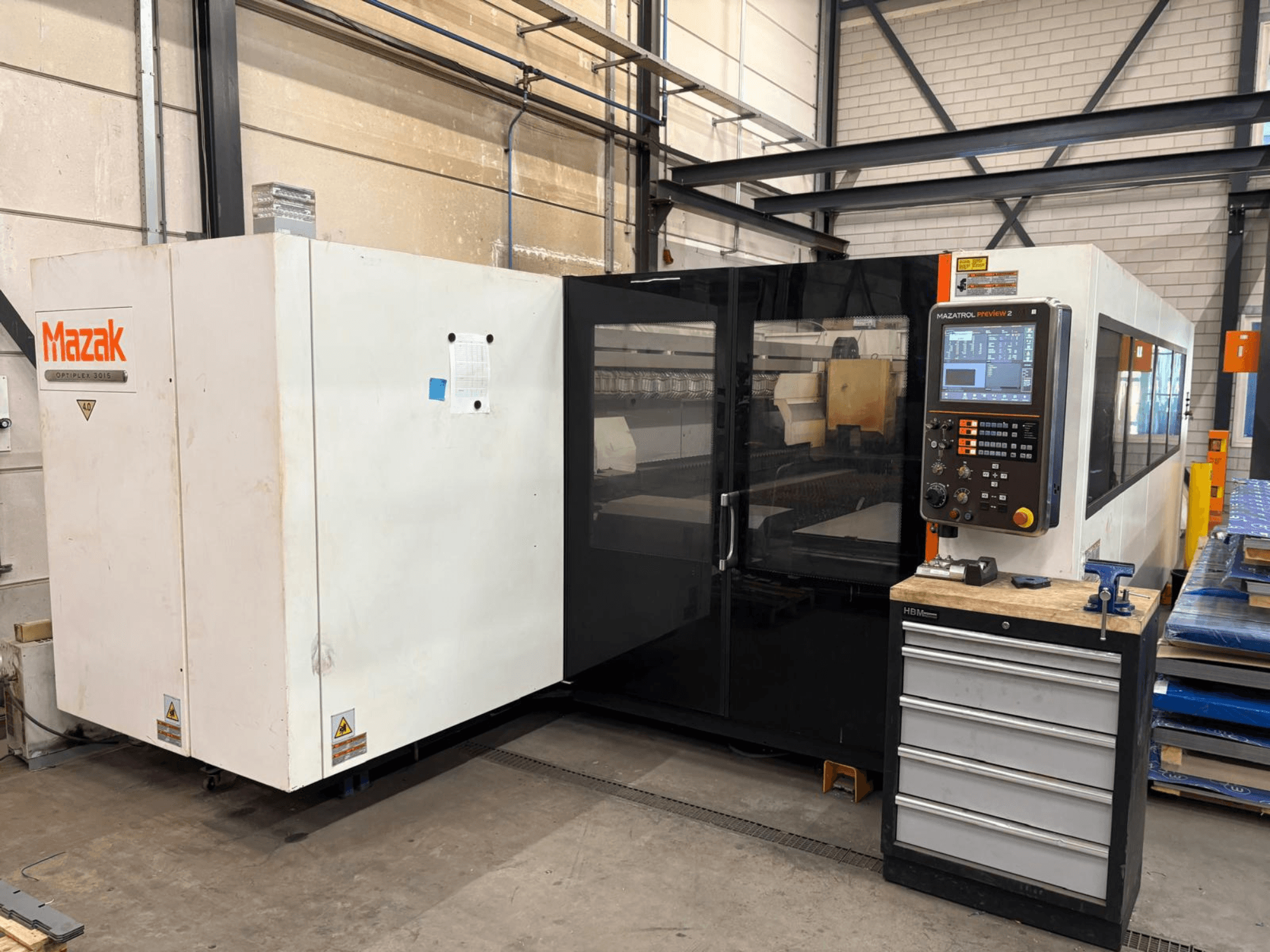 Mazak Optiplex 3015 CO₂-lézervágó gép, elölnézet, a vezérlőpanellel és az ipari környezettel.