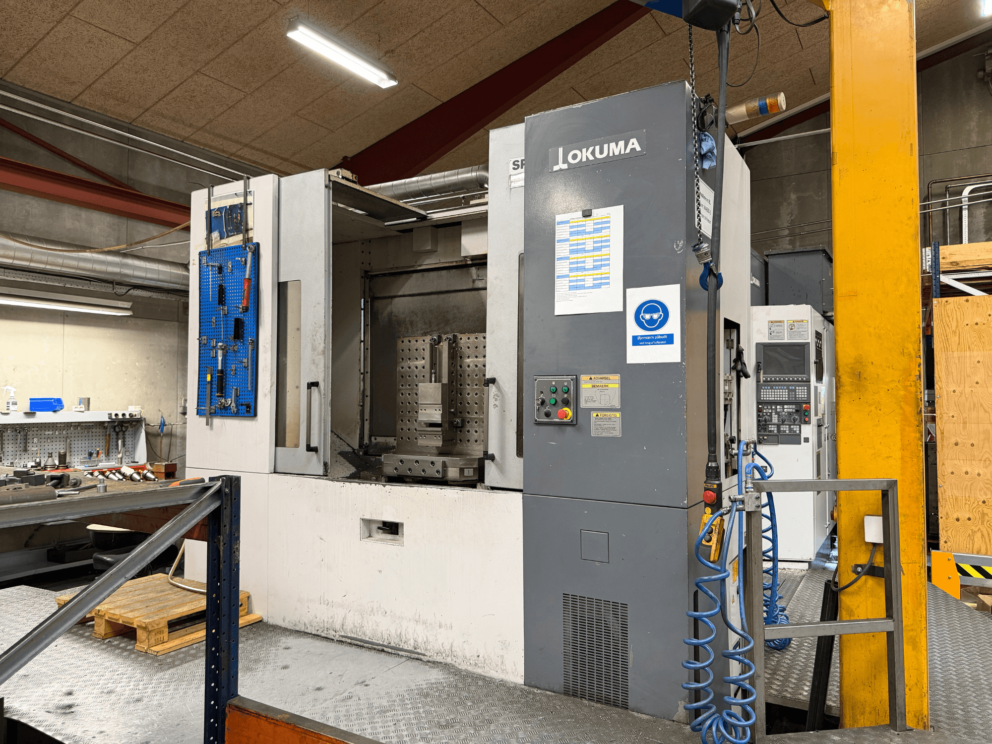 Okuma MA-600HB vízszintes megmunkálóközpont egy műhelyben, elölnézetből, a vezérlőpanellel és a munkaterülettel.