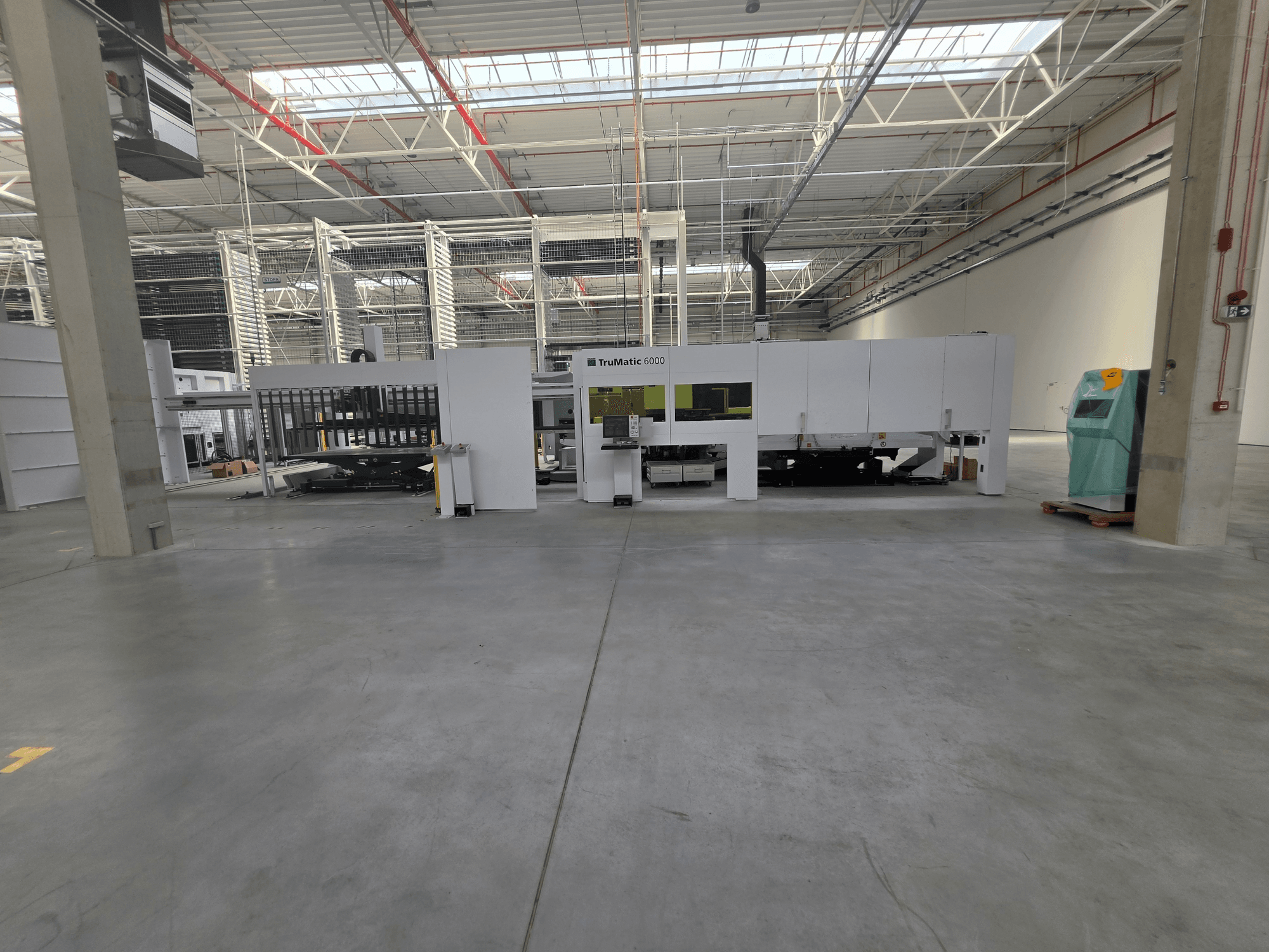 A TRUMPF TruMatic 6000-1600 száloptikás lyukasztó-lézer kombinált gép egy tágas raktárban, elölről nézve.