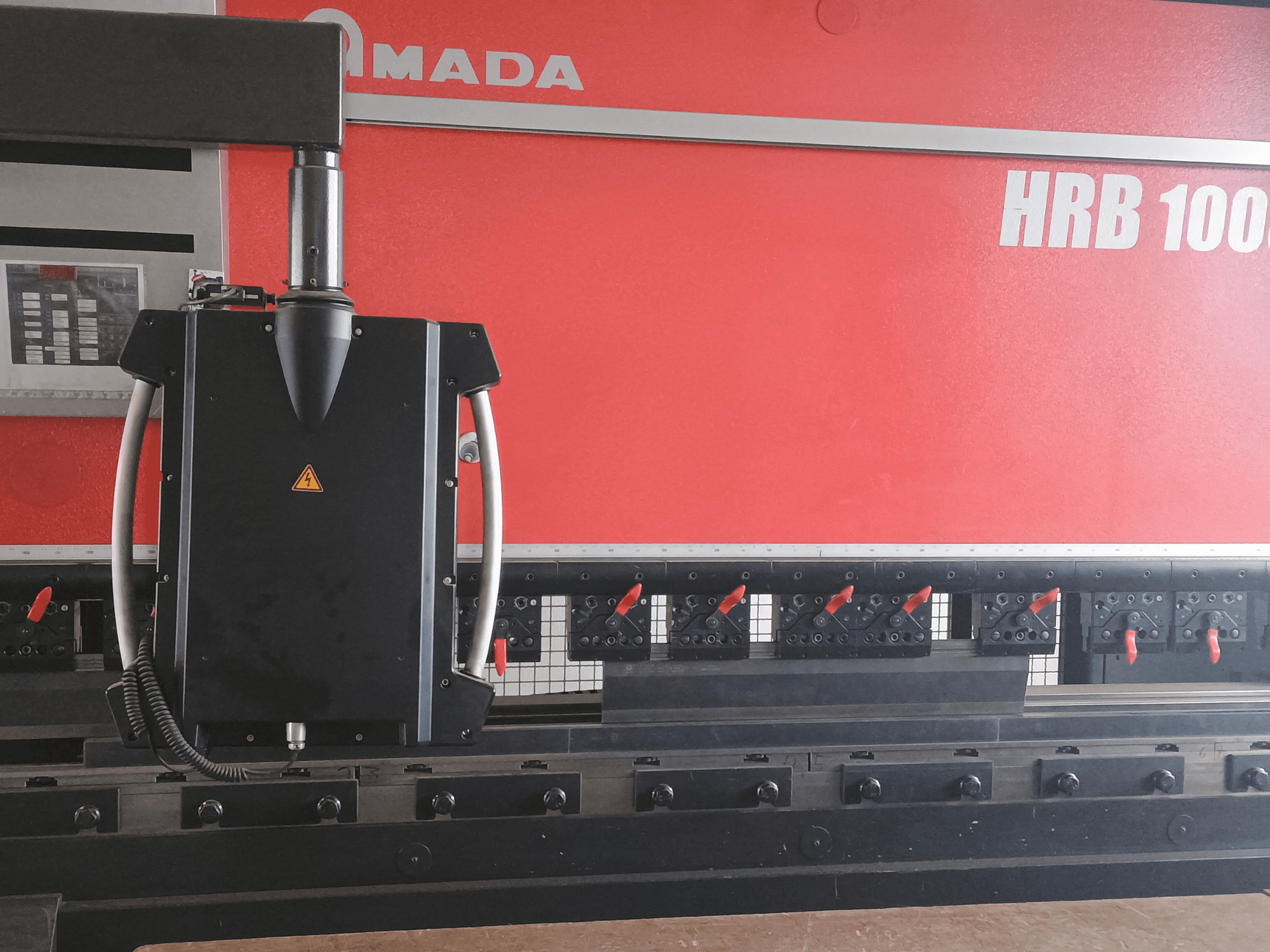 Amada HRB 100 hajlítógép elölnézetből; fekete vezérlőfej kúpos fúvókával és állítható szorítókkal.