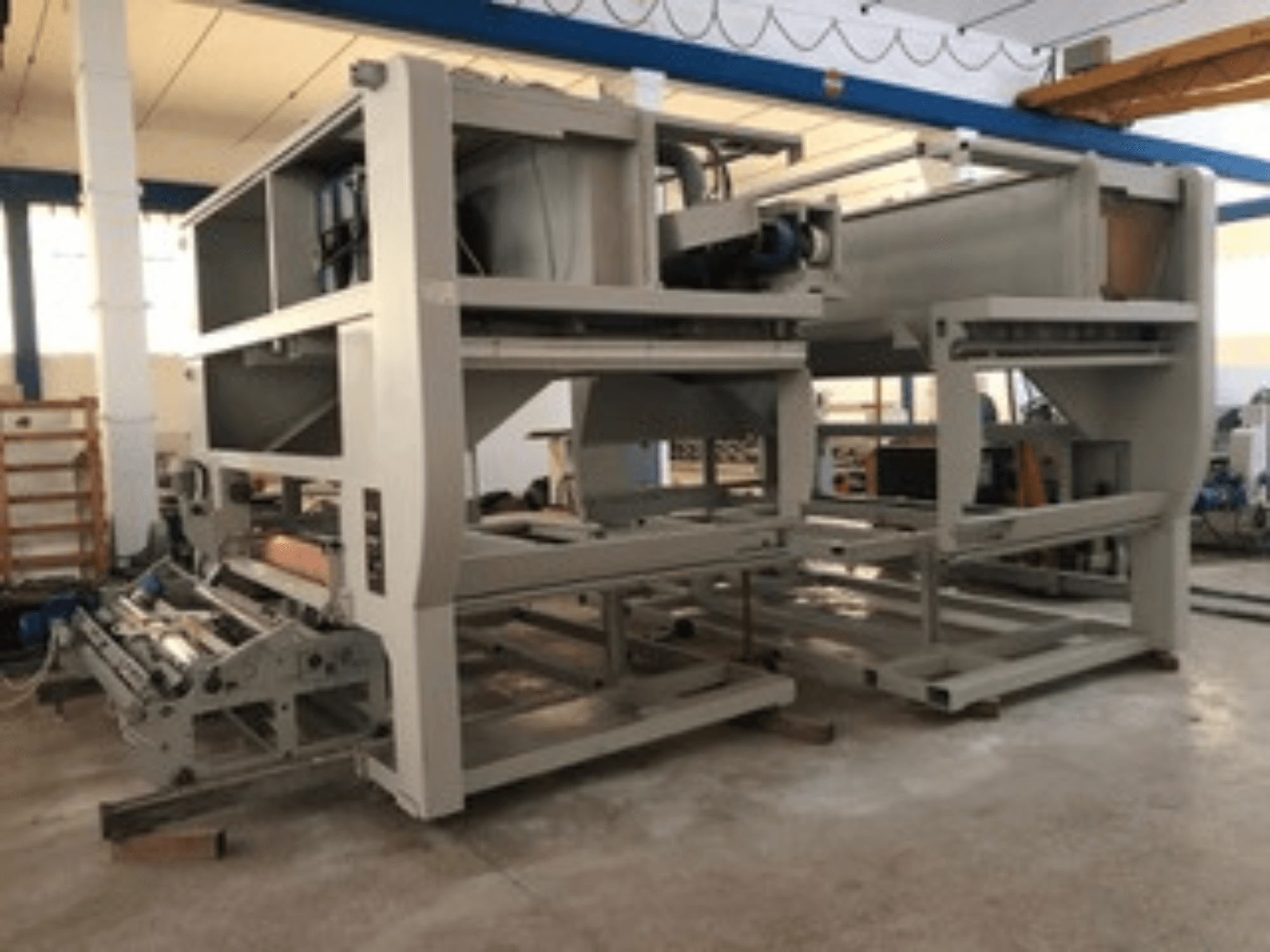 Ipari gép több szállítógörgővel és nagy szerkezettel; oldalnézet, szürke szín, jól megvilágított gyárban található.