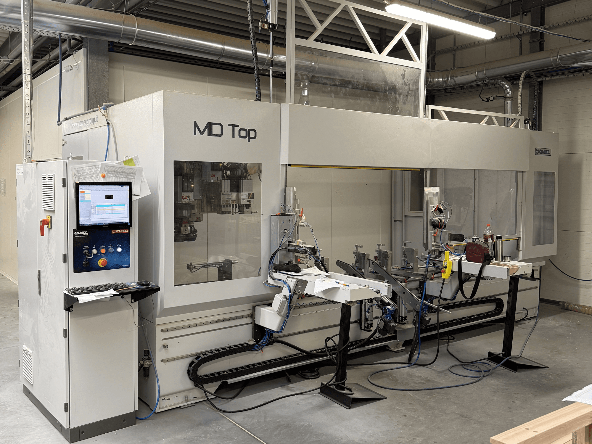 MD Top CNC-gép szemből nézve, a vezérlőpanel, a robotkarok, valamint a szerszámokkal és anyagokkal ellátott munkaterület.