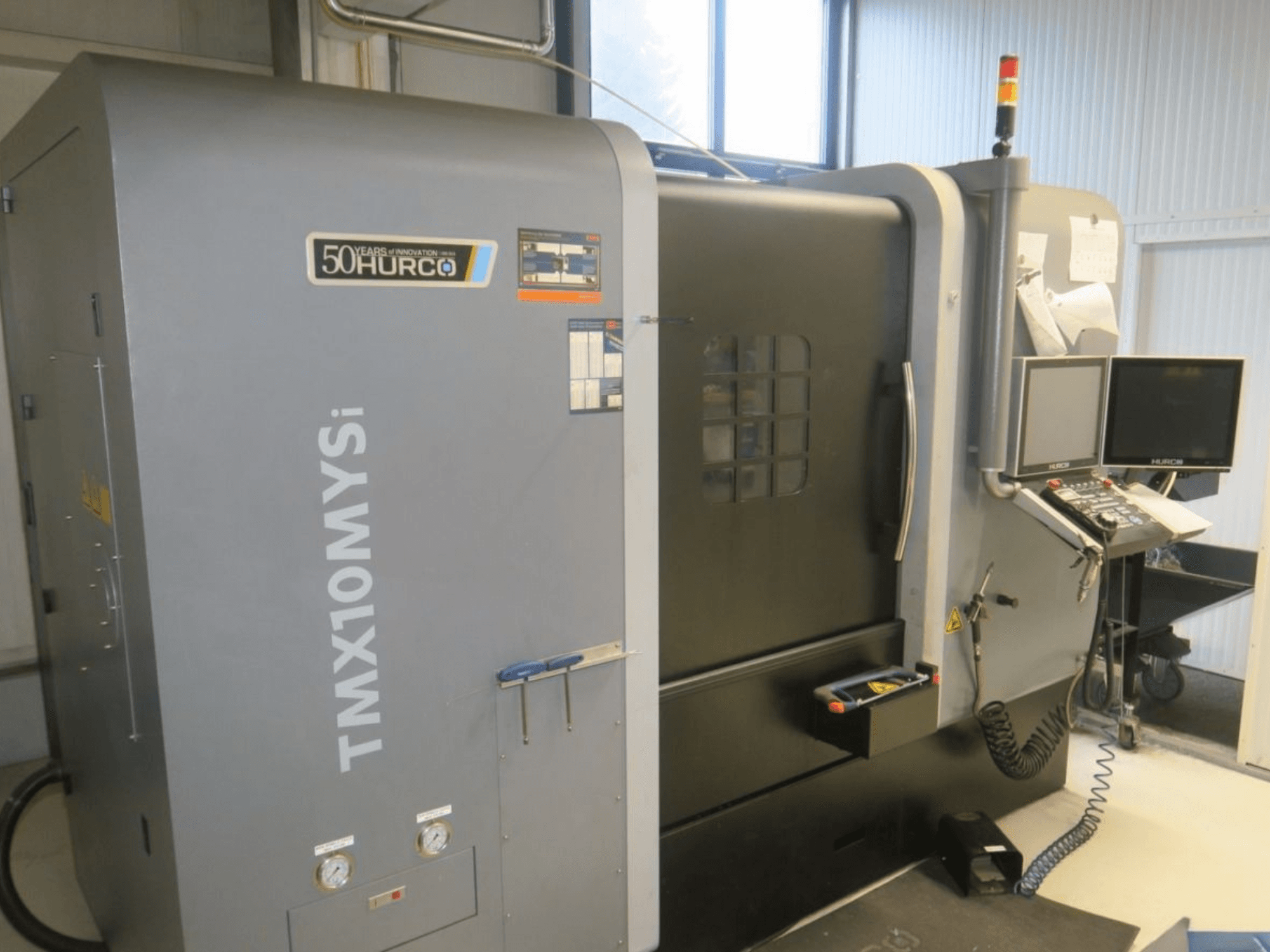 Hurco TMX10MYSi CNC-gép oldalnézetben; vezérlőpanel, vészvillogók és kijelzett műszerek.