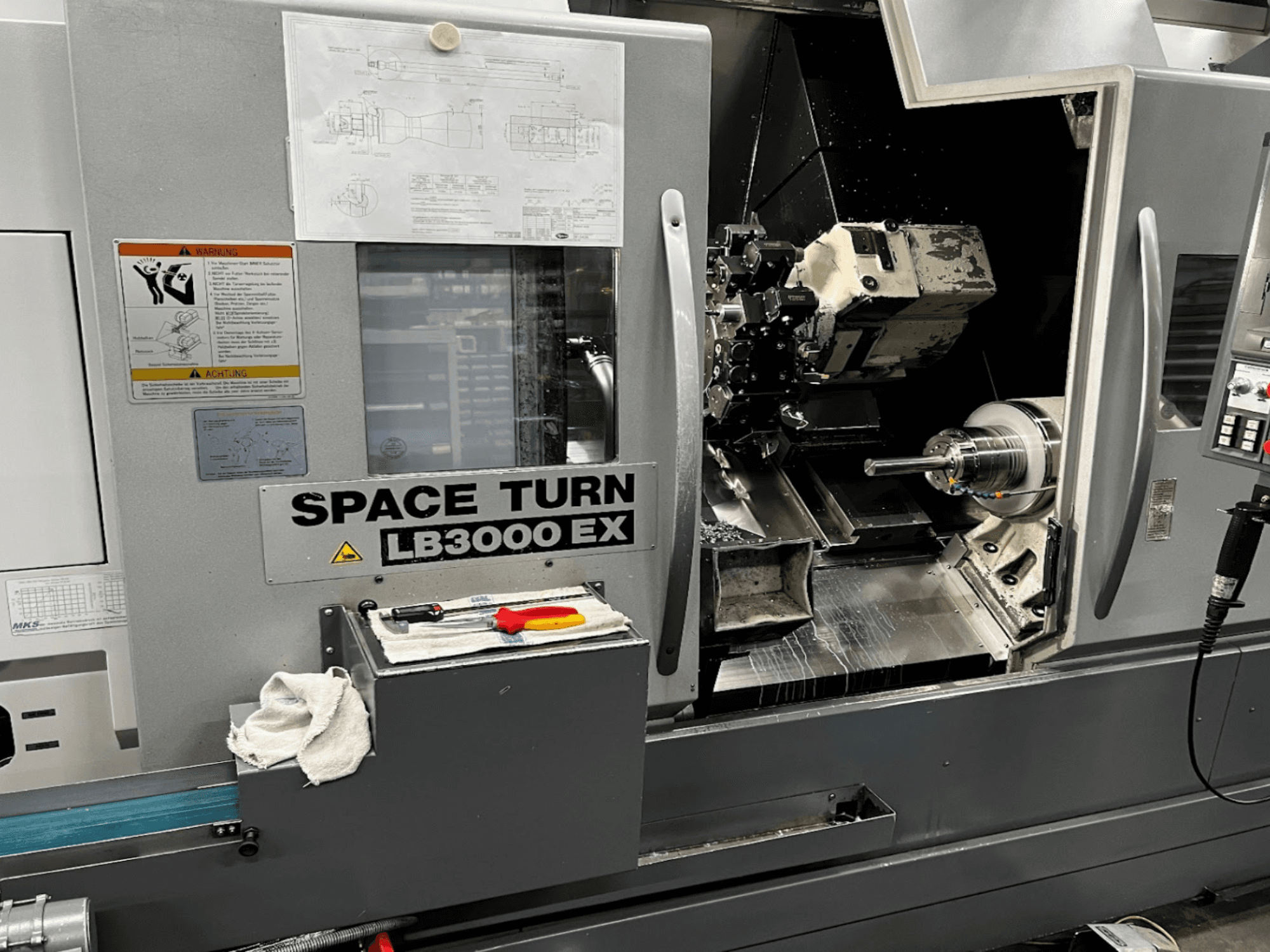 Okuma LB3000EX MYW vízszintes esztergagép, elölnézet a vezérlőpanel, a szerszámok és a munkaterület részletei láthatóak.